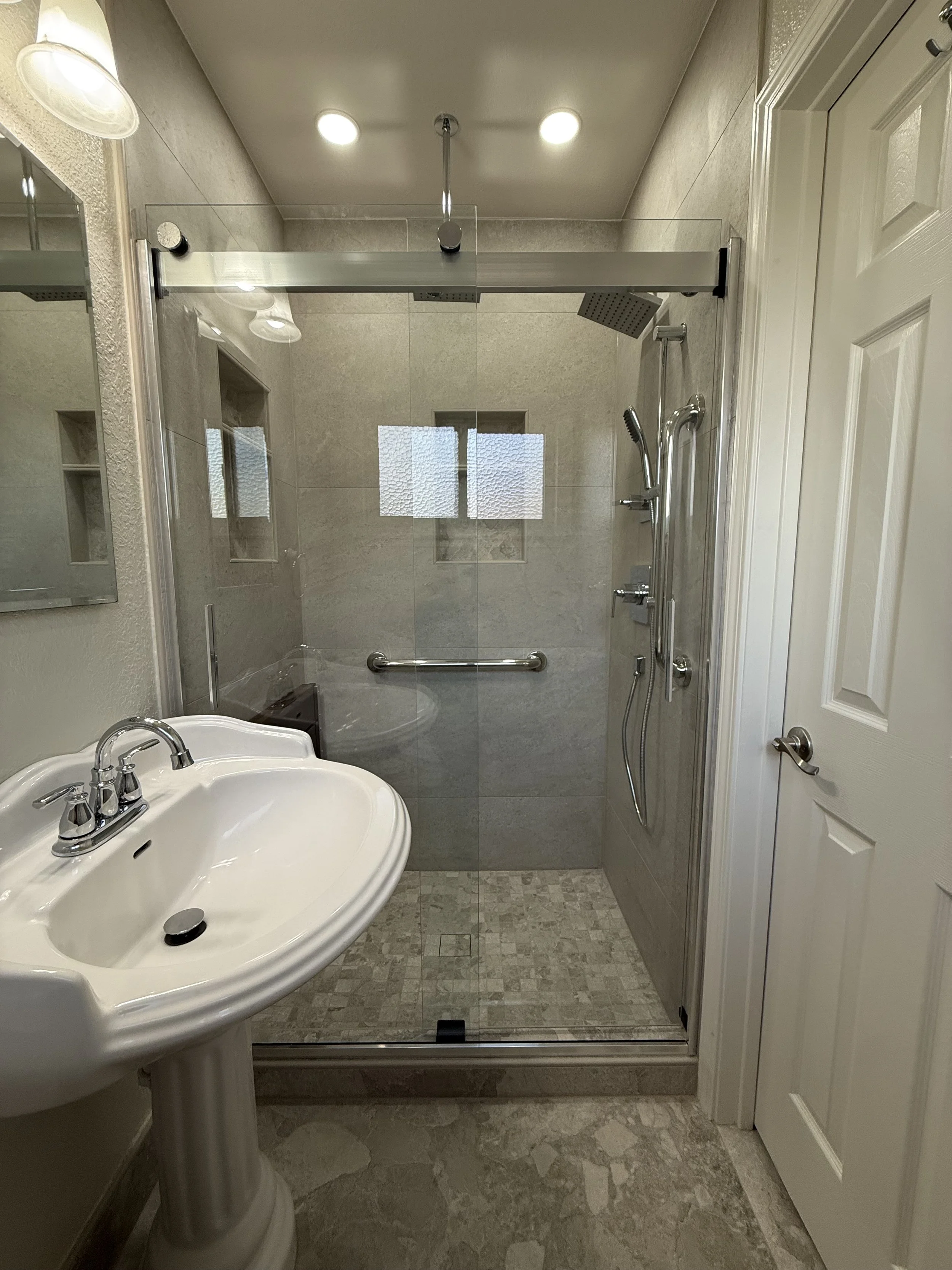 Bathroom with a glass shower stall, a white pedestal sink, and a door to the right.