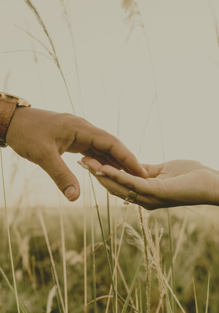 Close-up of two hands almost touching in a field, representing relationship therapy and pattern work for women in New York City.