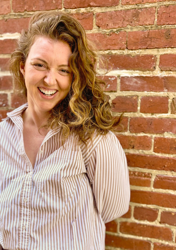 Kelsey Dunn, LMHC, somatic therapist in New York City, standing against a brick wall.