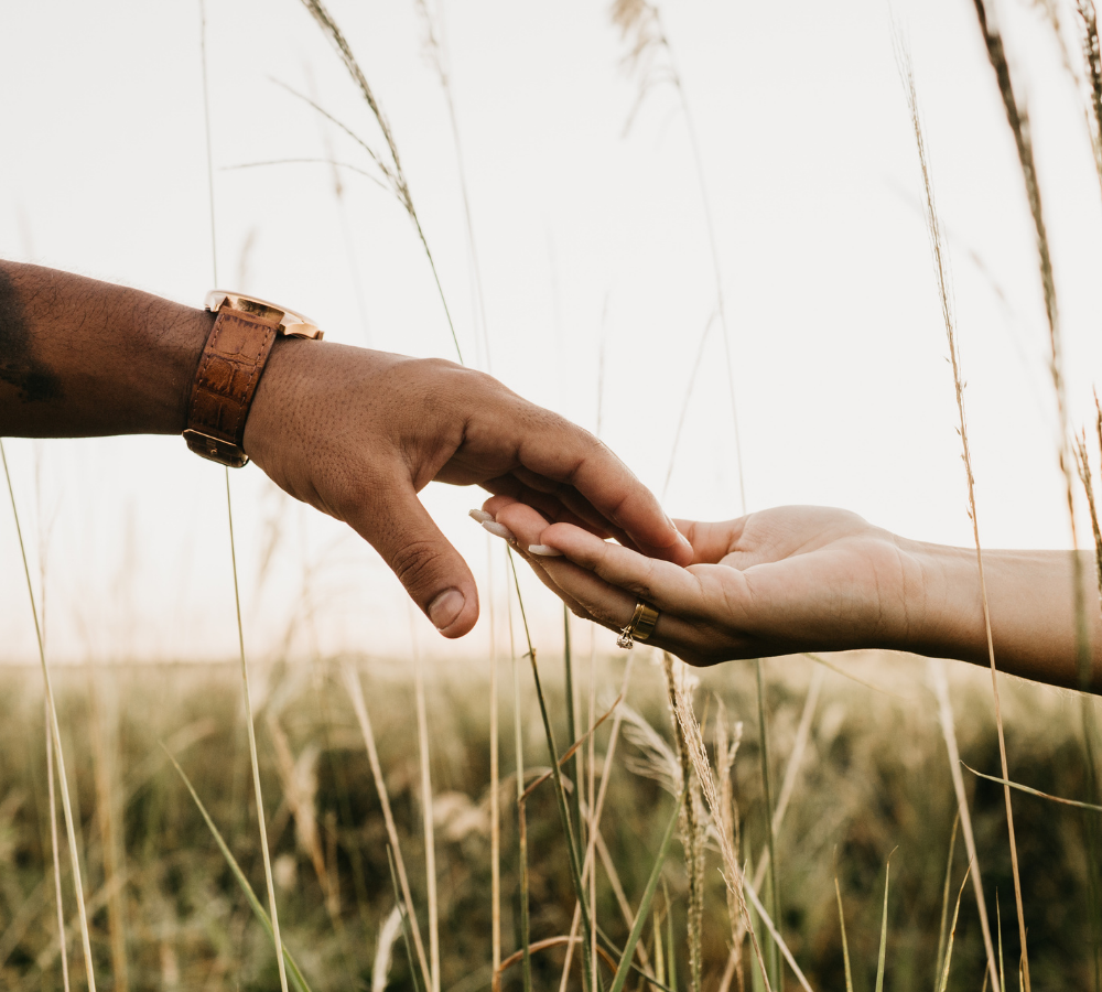 Close-up of two hands almost touching in a field, representing relationship therapy and connection for women in New York.