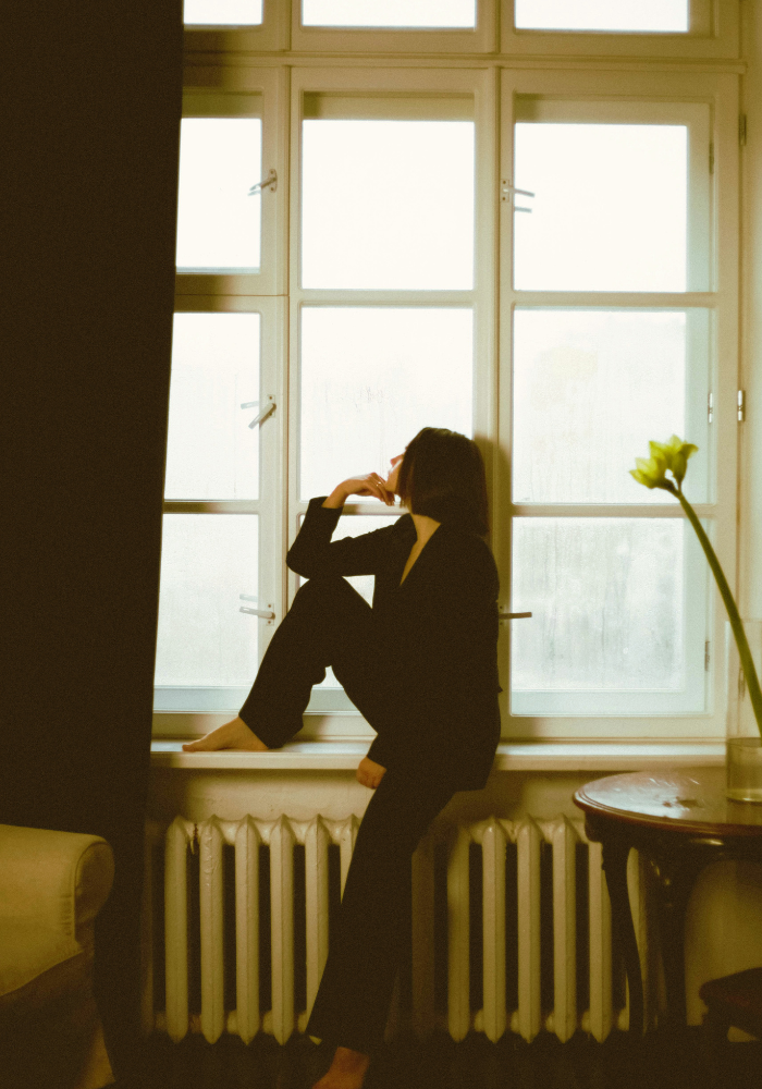 Woman in black sitting by a window, representing somatic therapy for anxiety, burnout, and overwhelm for women in New York City.