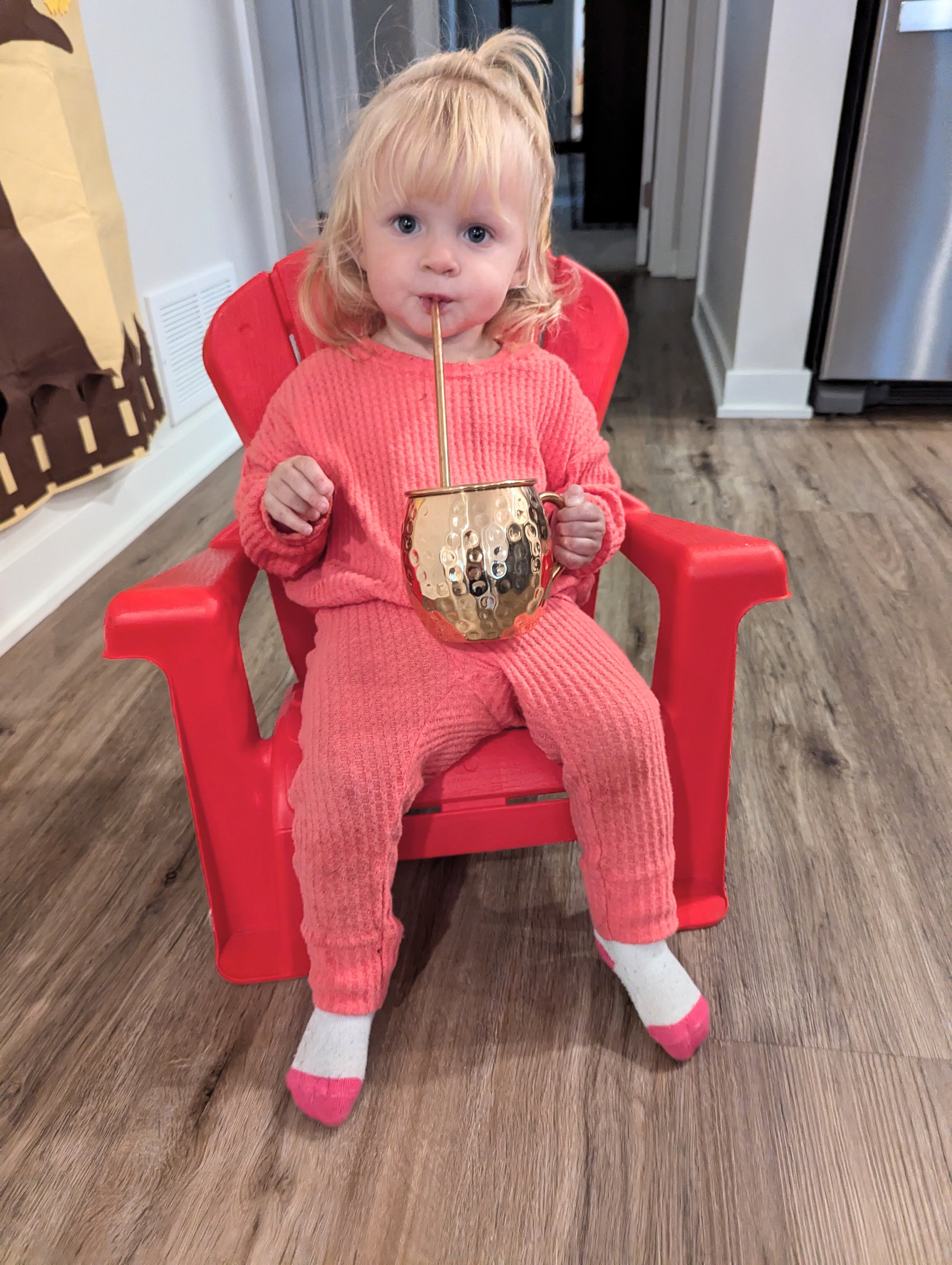 Toddler in red chair sipping out of copper mug