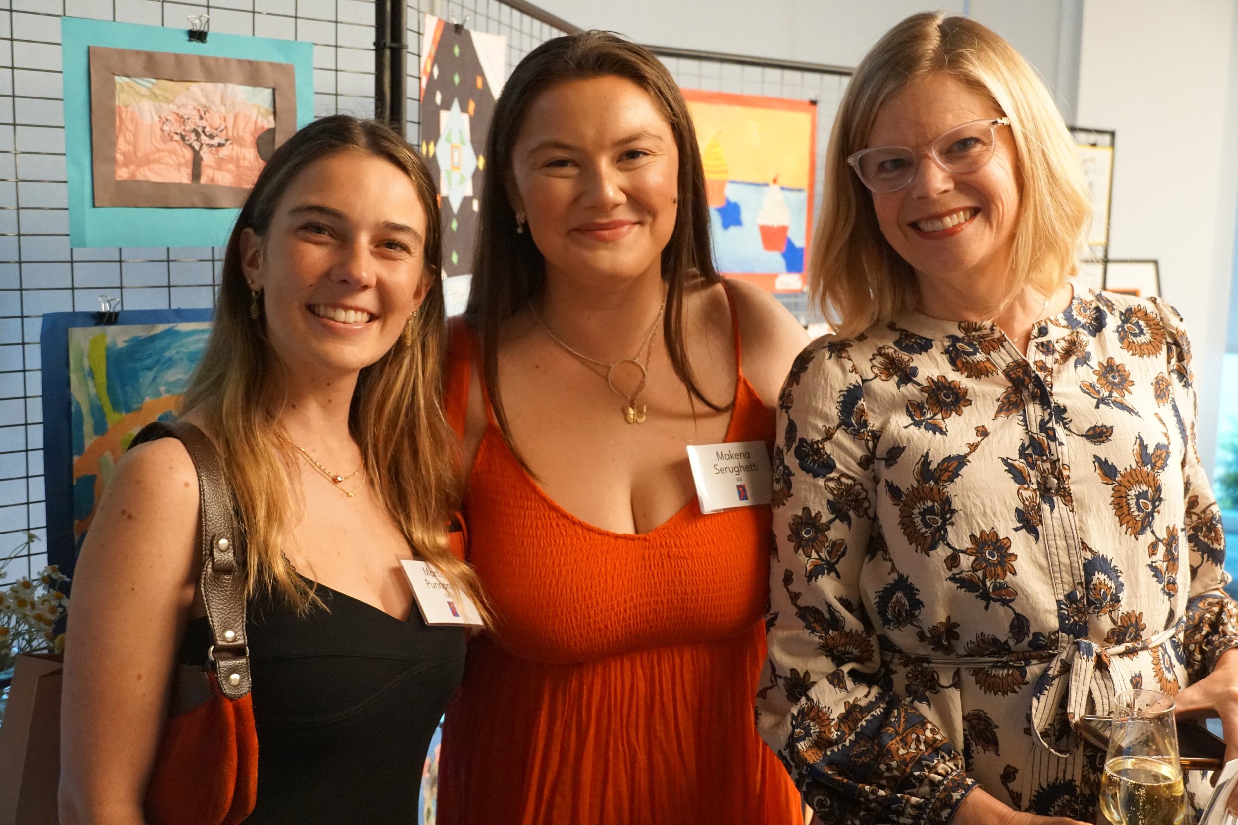three woman smiling in front of children's art