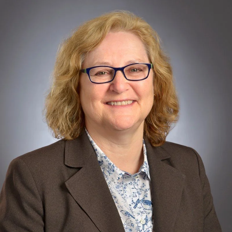 Susan Ball headshot, she is smiling with black eyeglasses  and a button up shirt