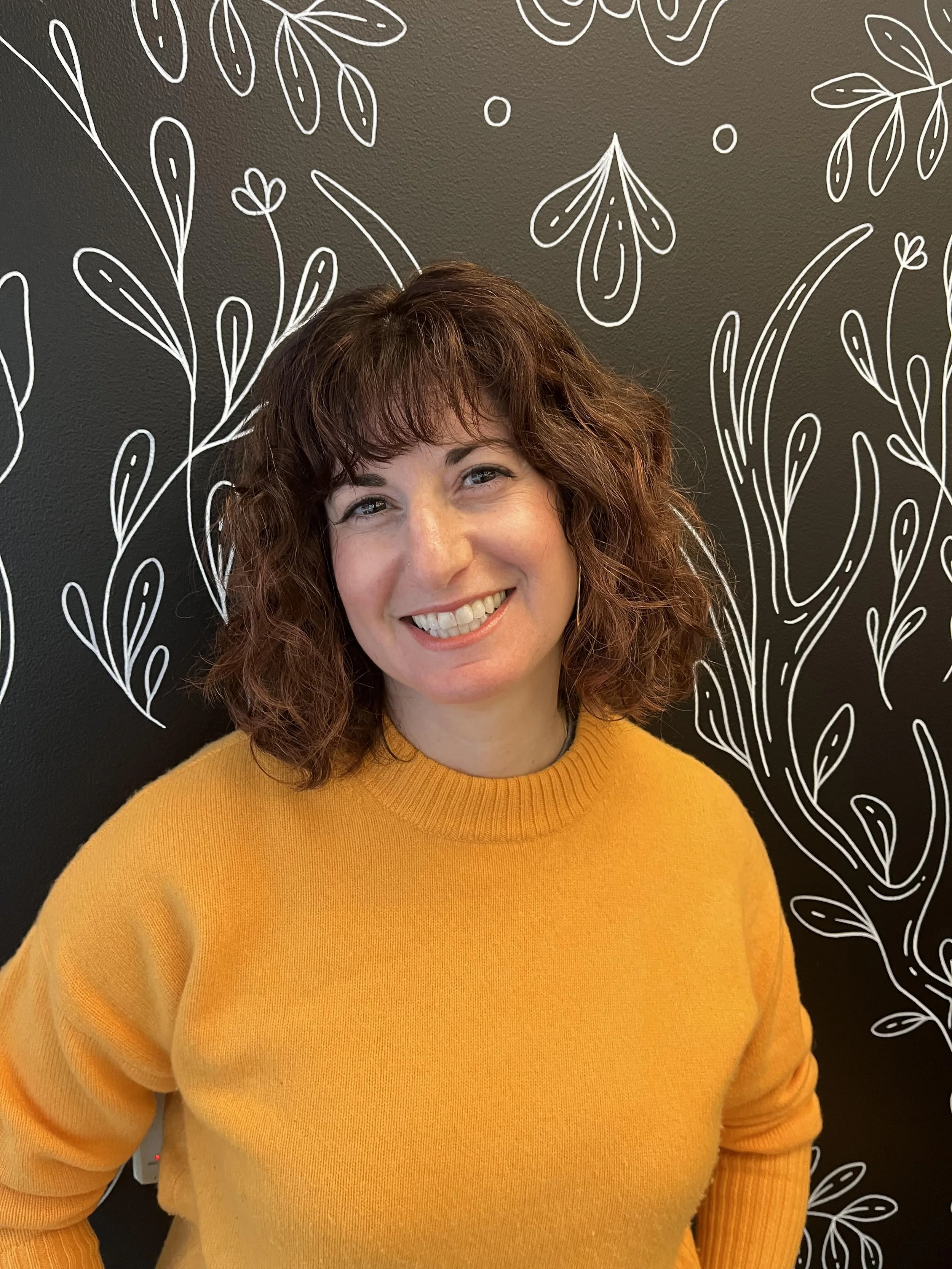 Julia Capeloto headshot with her smiling in an orange sweater