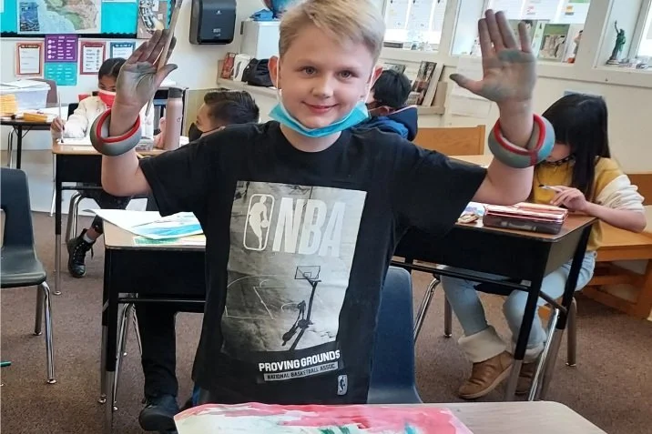student smiling with his hands up and art on the table