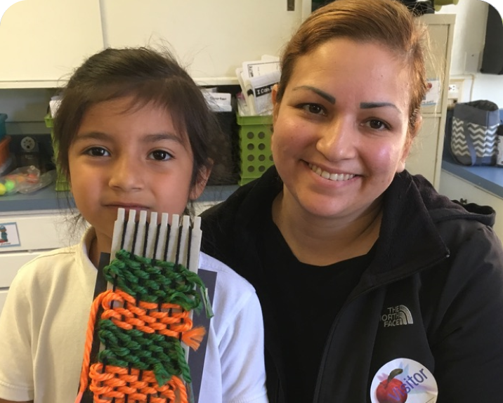 young girl on the left with a orange and green knit project in hand and her mother visting with a smile on her face