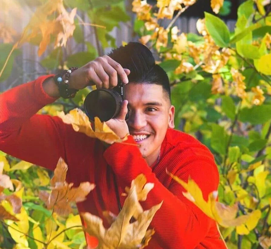 Man in a red sweater who goes by the name Christian holding a camera smiling