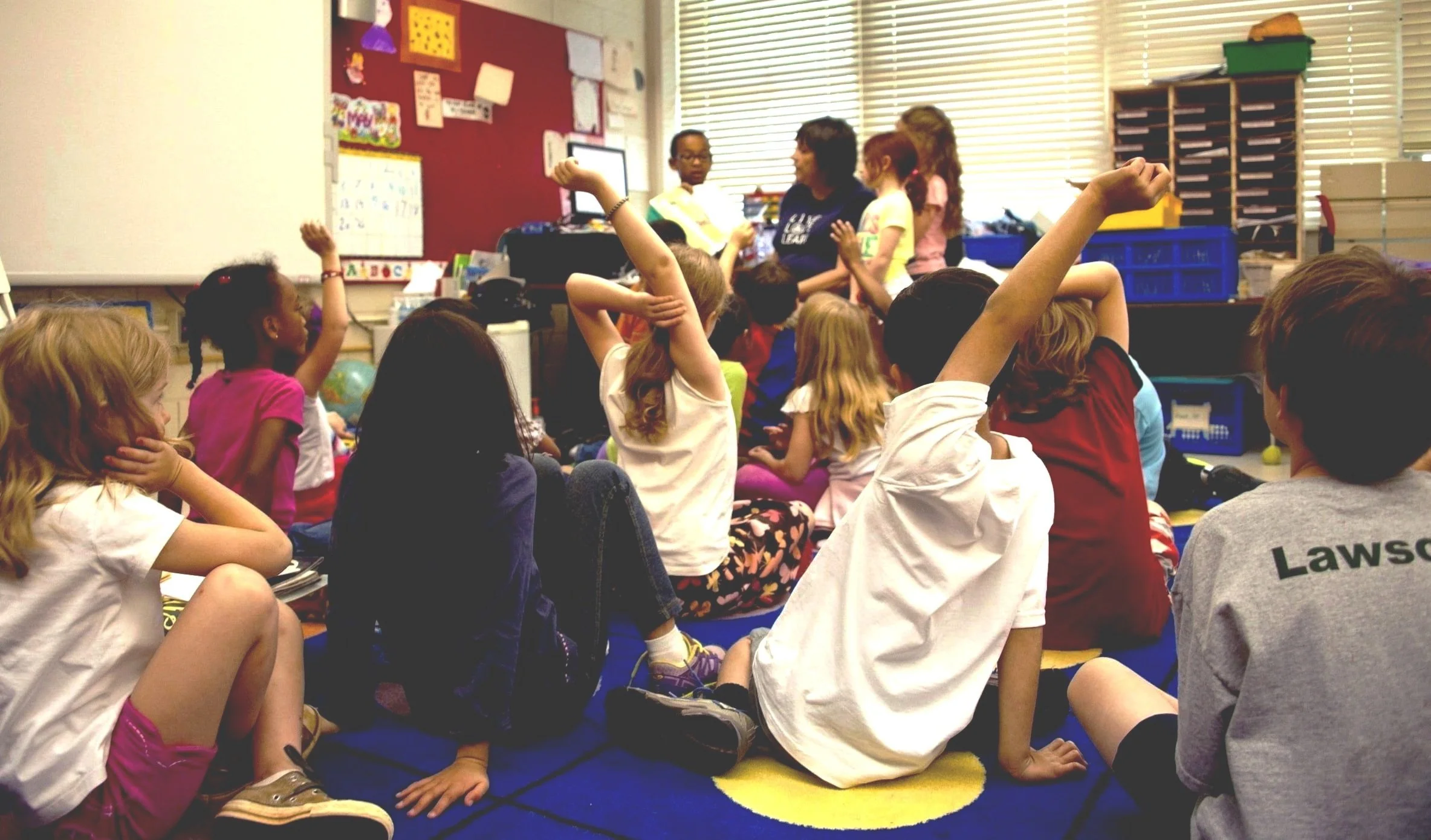 student presenting art to peers sitting on a carpet floor