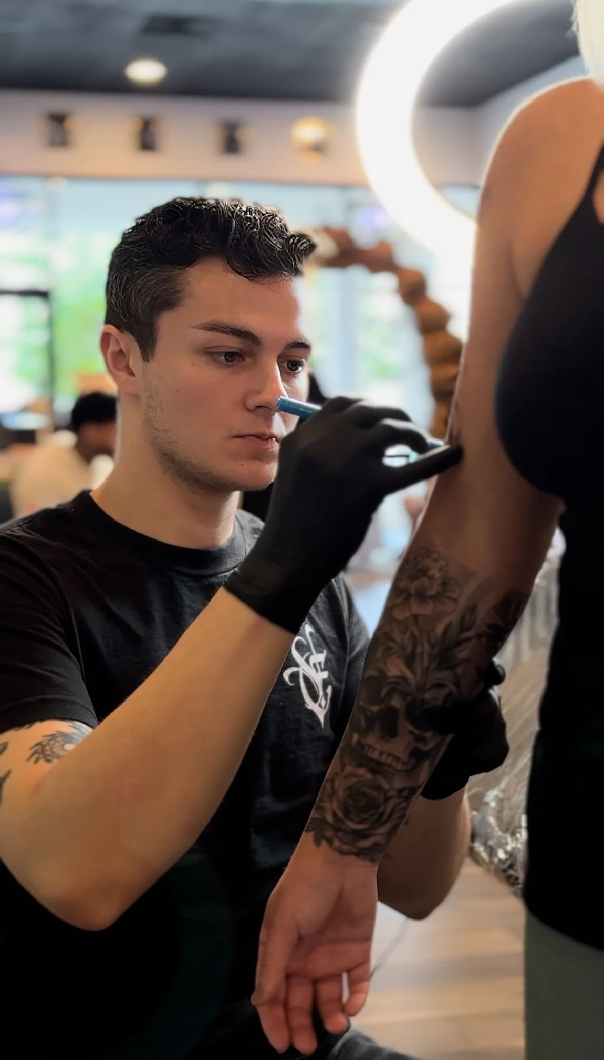 Tattoo artist with gloves applying a stencil on a person's arm with tattoos in a studio environment.