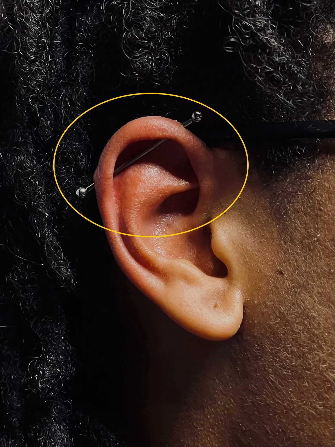 Close-up of a person's ear with an industrial bar piercing.
