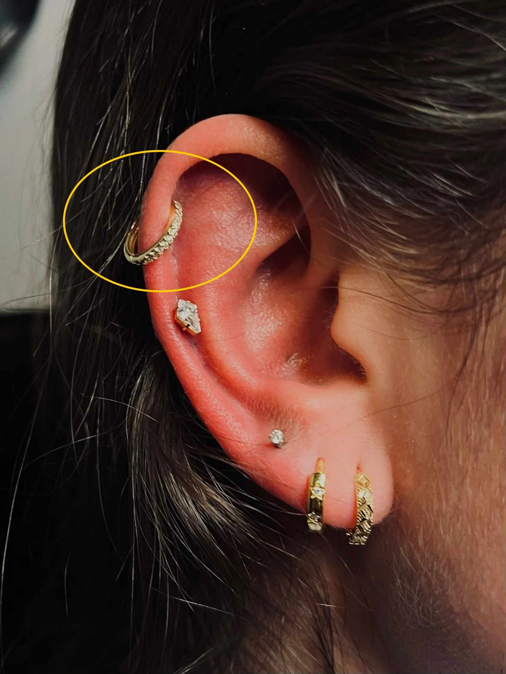 Close-up of an ear with multiple piercings, including gold hoops and studs.