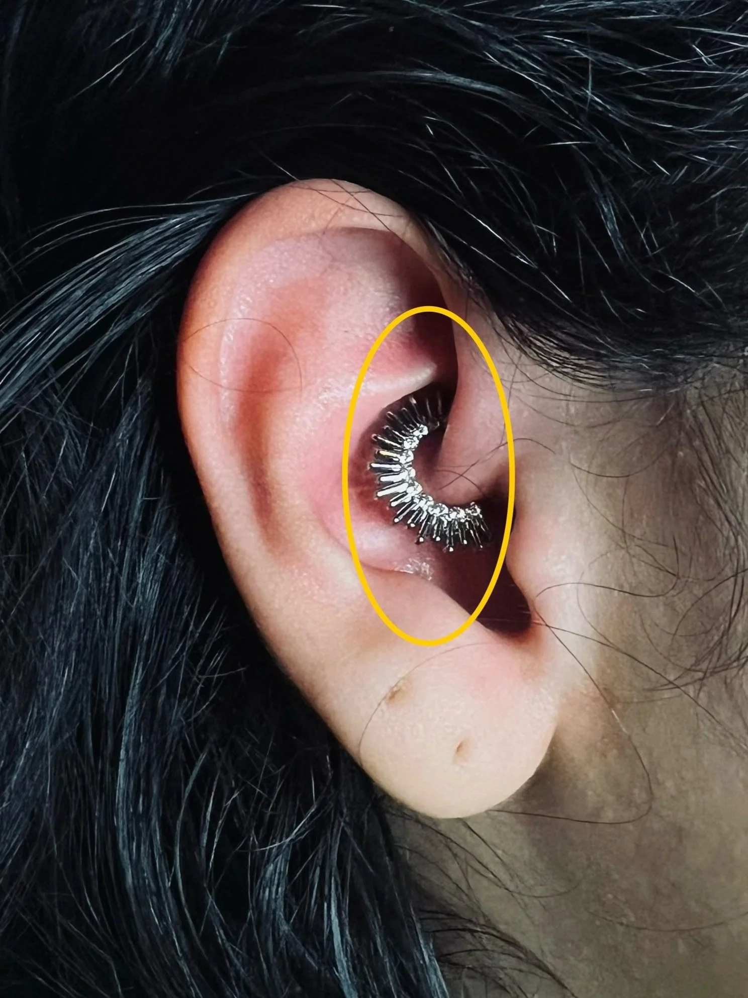 Close-up of a human ear with a silver spike-patterned ear cuff.
