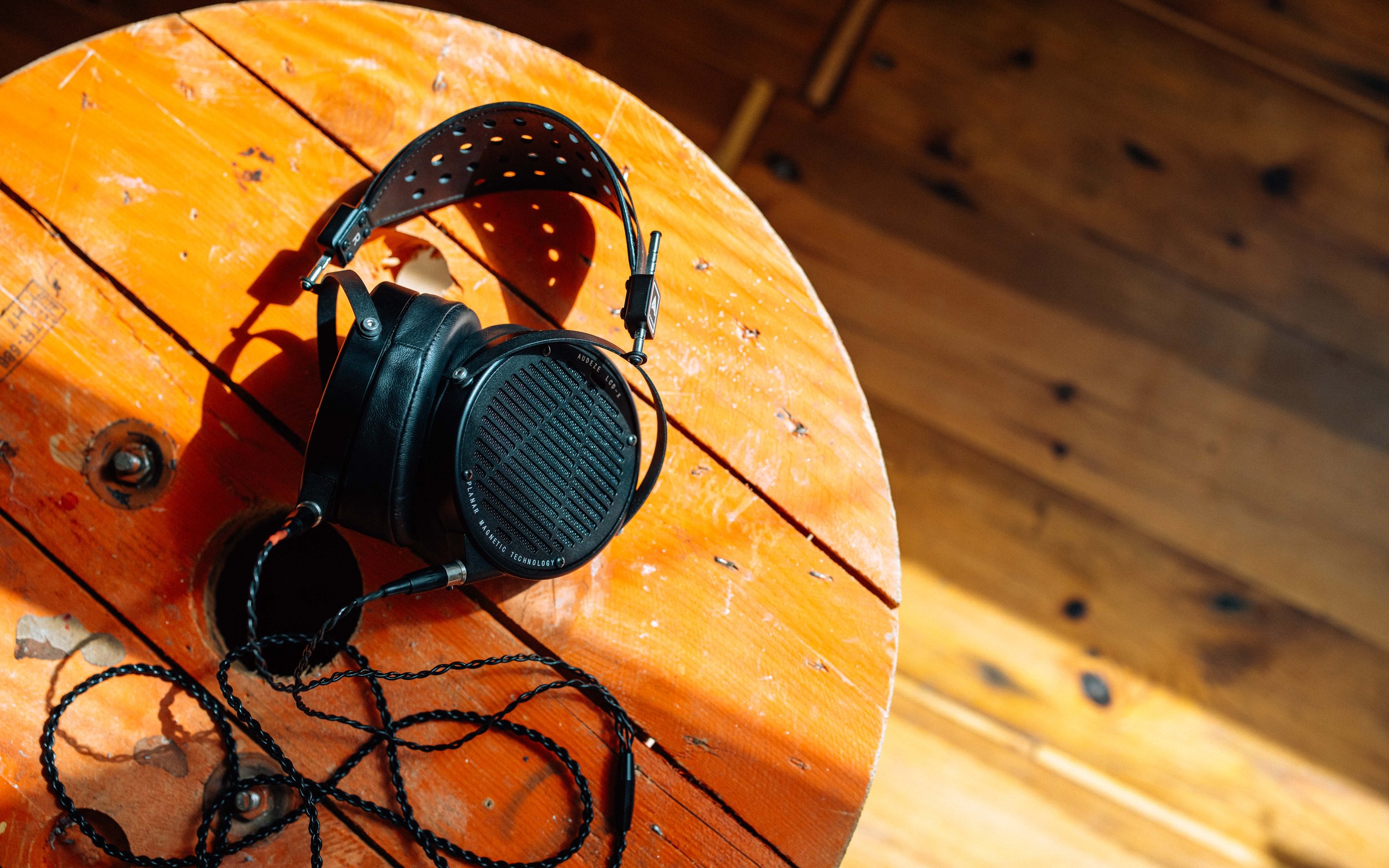 A pair of black over-ear headphones with a braided cable resting on a round, orange wooden table with visible grain and scratches.