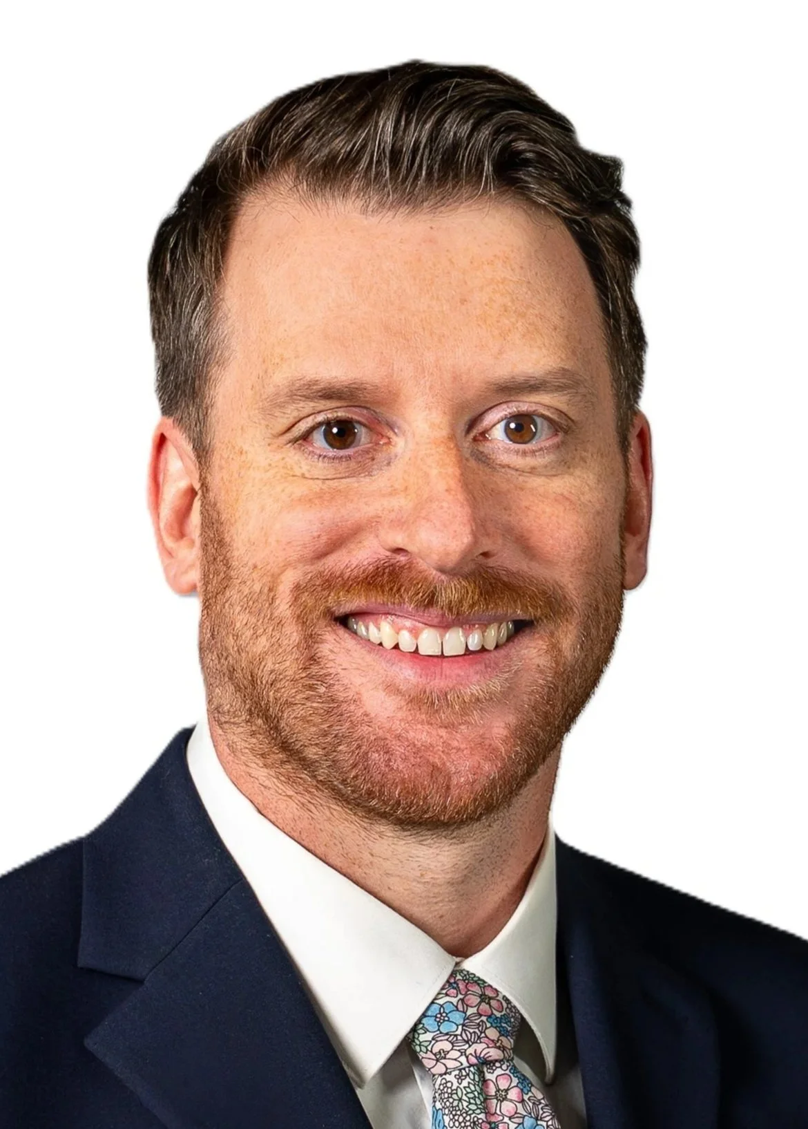 Close-up of a smiling man with brown hair, a beard, wearing a blue jacket and white shirt.