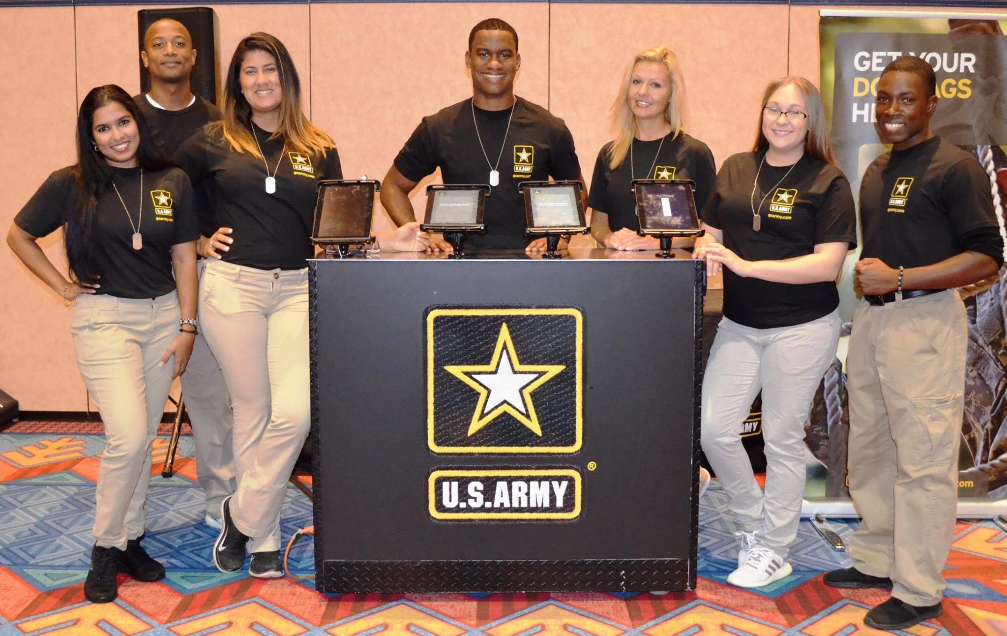 Diverse group of U.S. Army brand ambassadors and event staff in black t-shirts posing around a branded booth with tablets - Event Staffing Live
