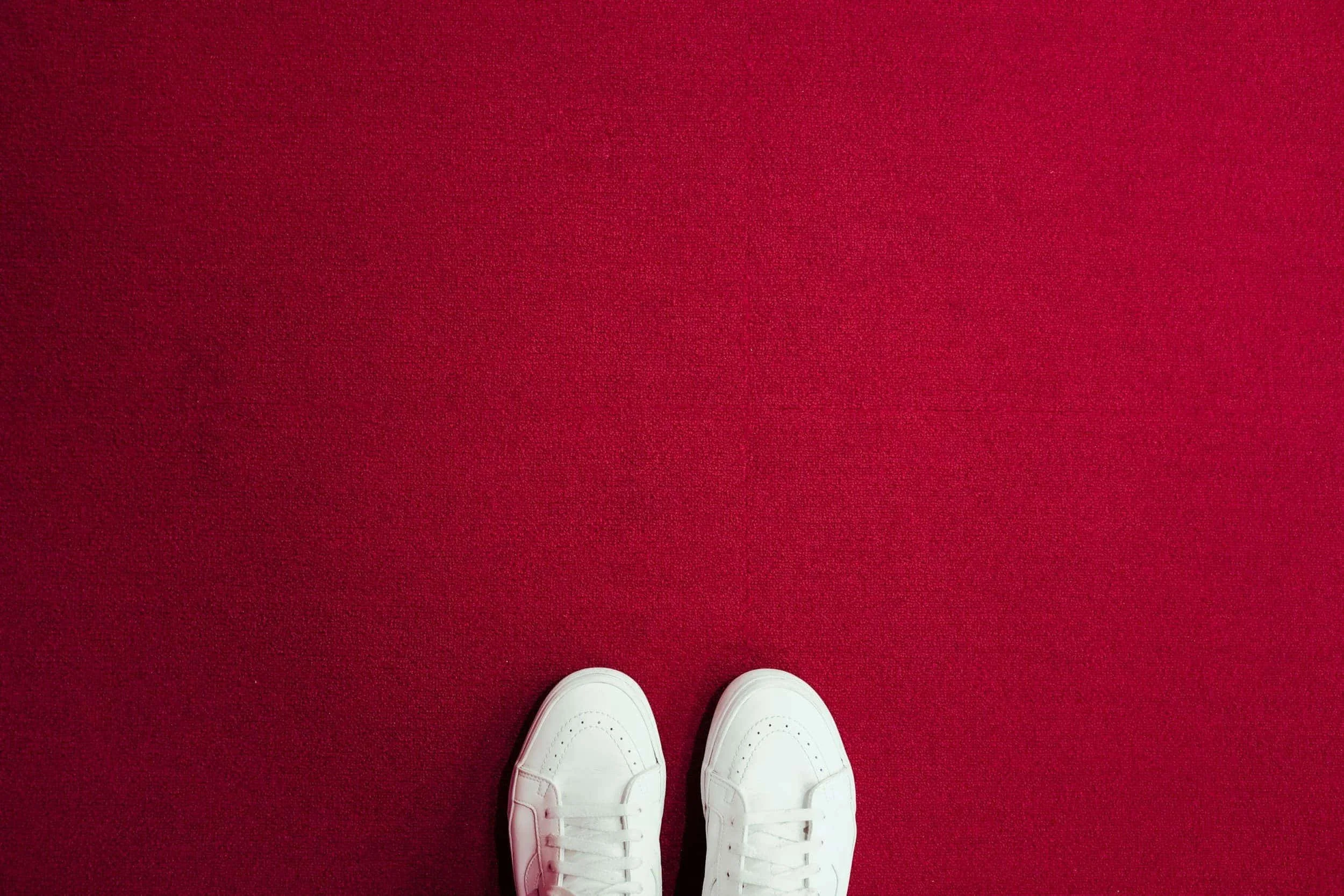 Top-down view of white leather sneakers standing on a bright red carpet background