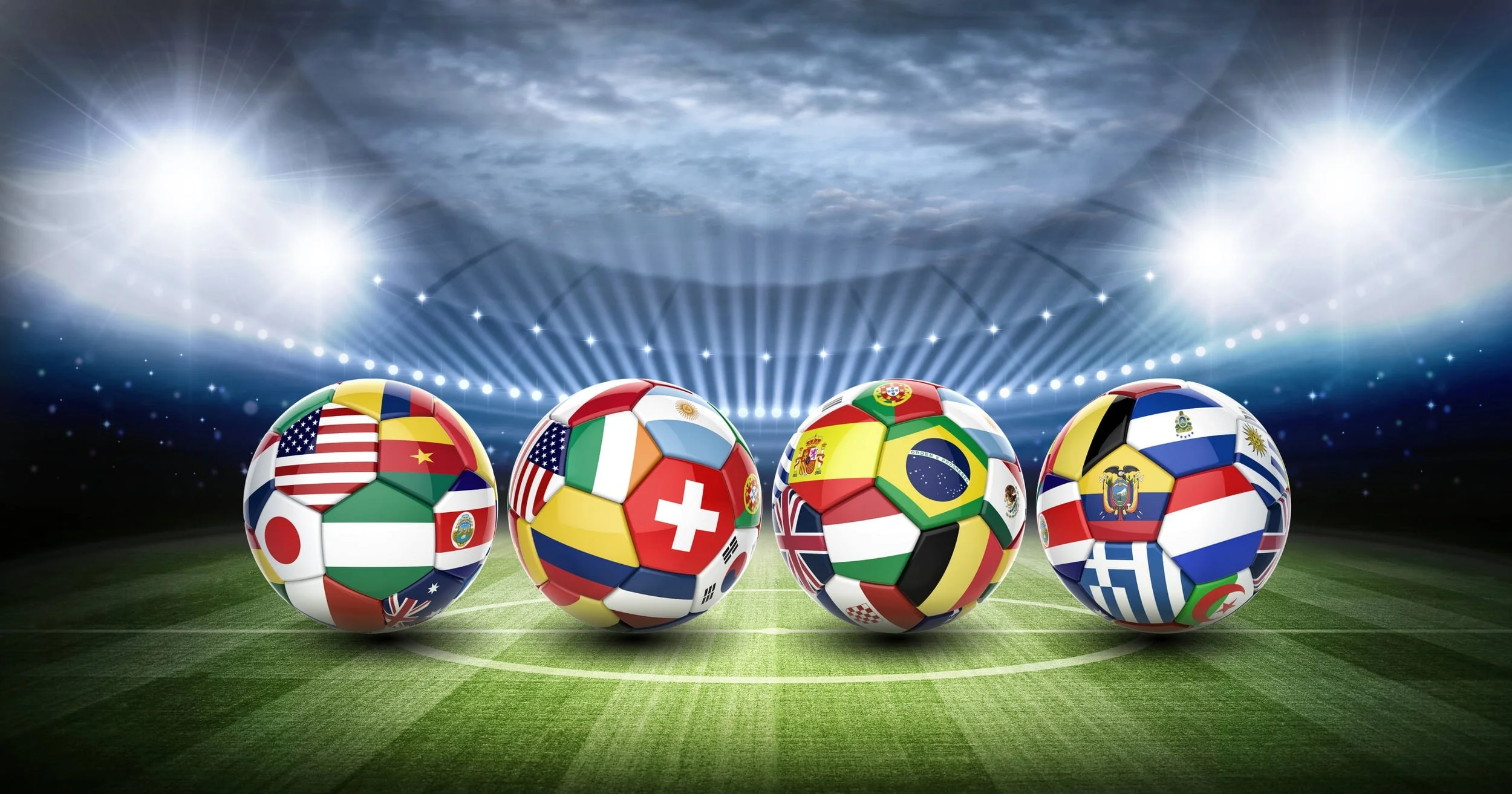 Four soccer balls featuring various international country flags lined up on a lit stadium pitch field - Event Staffing Live