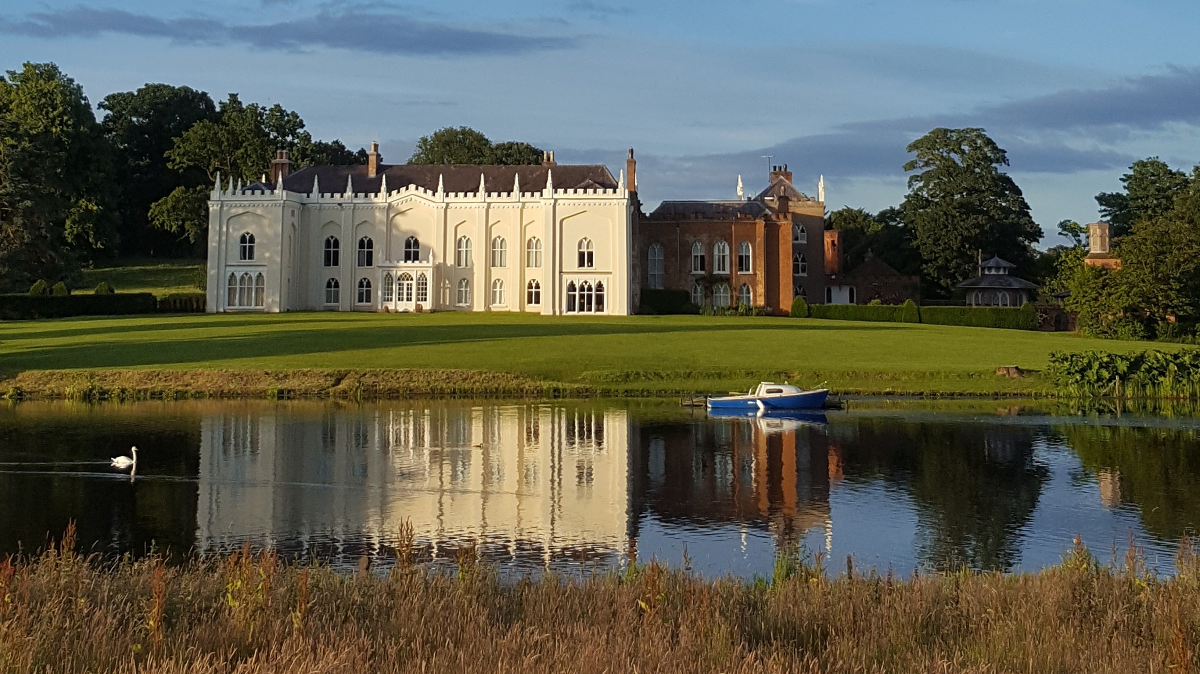 Cheshire Wedding Videographer, combermere abbey with a reflection on the building in the lake on a sunny day