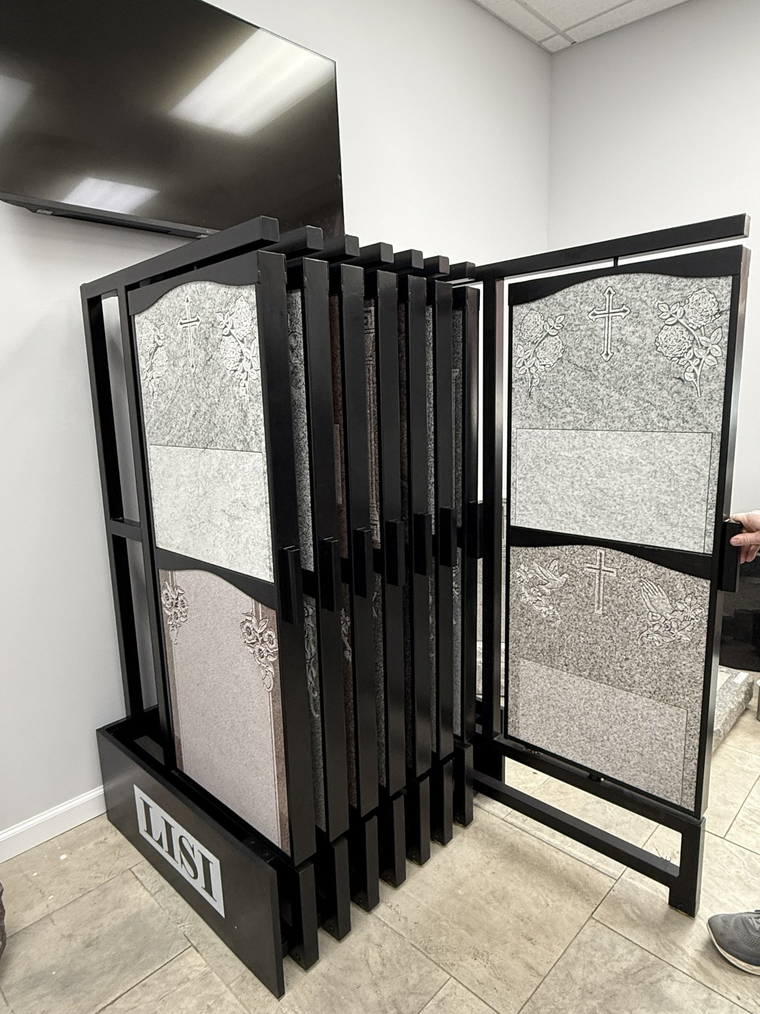 A black metal frame on wheels holding granite headstones with floral and cross designs, used for display in a showroom.