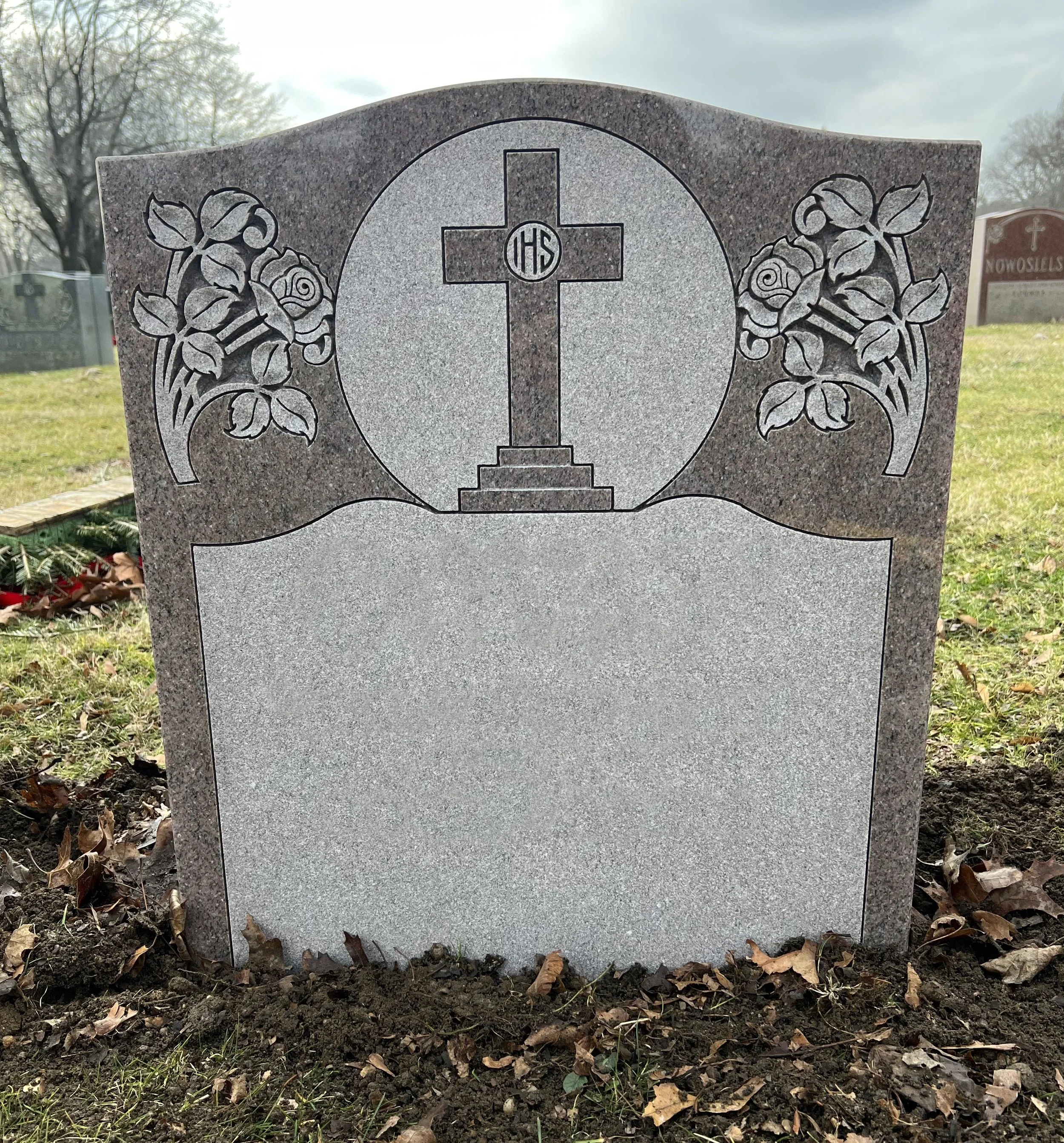 Gravestone with a cross and roses carved into the top, blank inscription area.