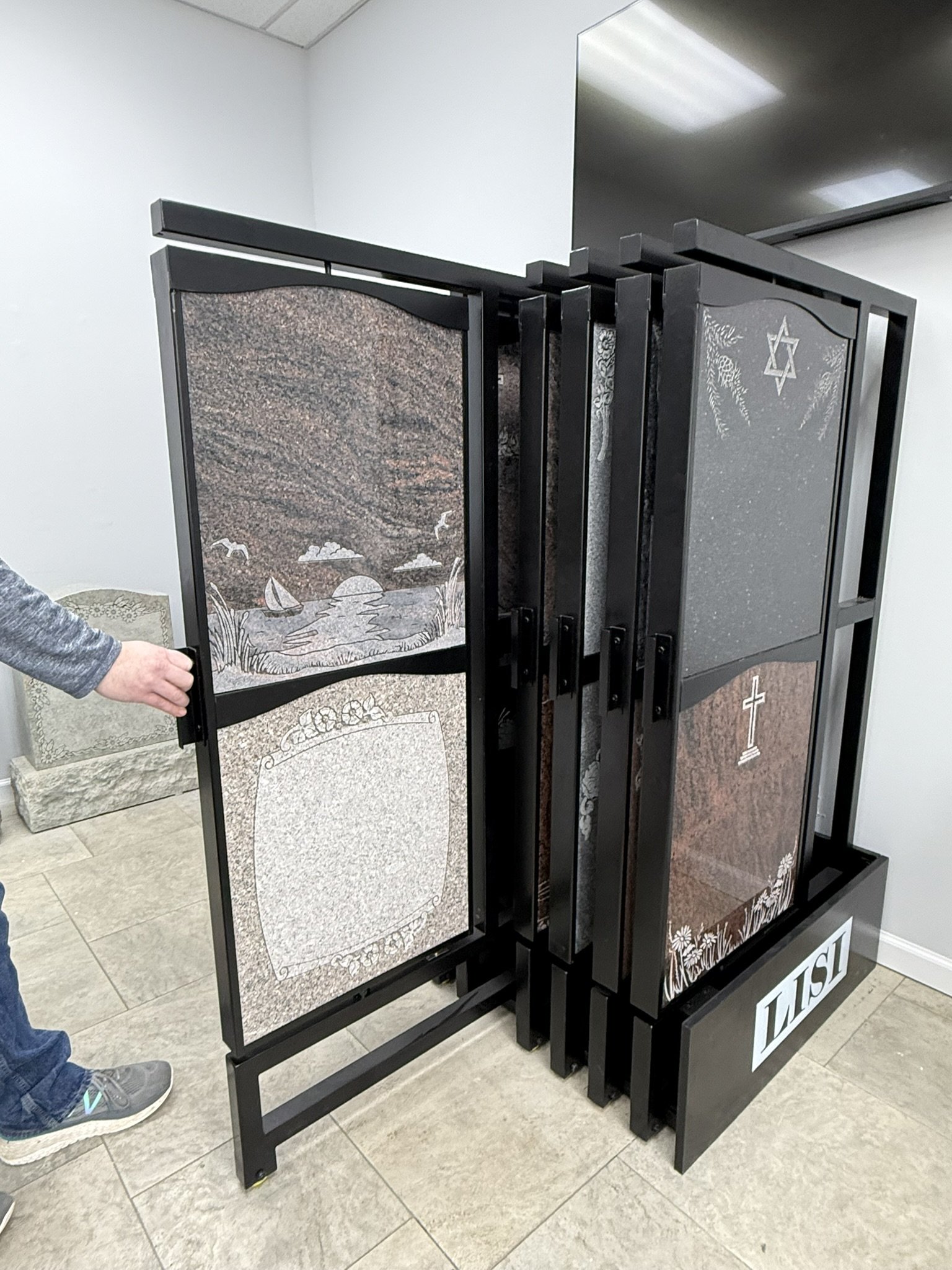 A black folding altar with religious and nature-themed engravings, including a star of David, a cross, and natural scenery, on a gray tiled floor in a room with white walls.