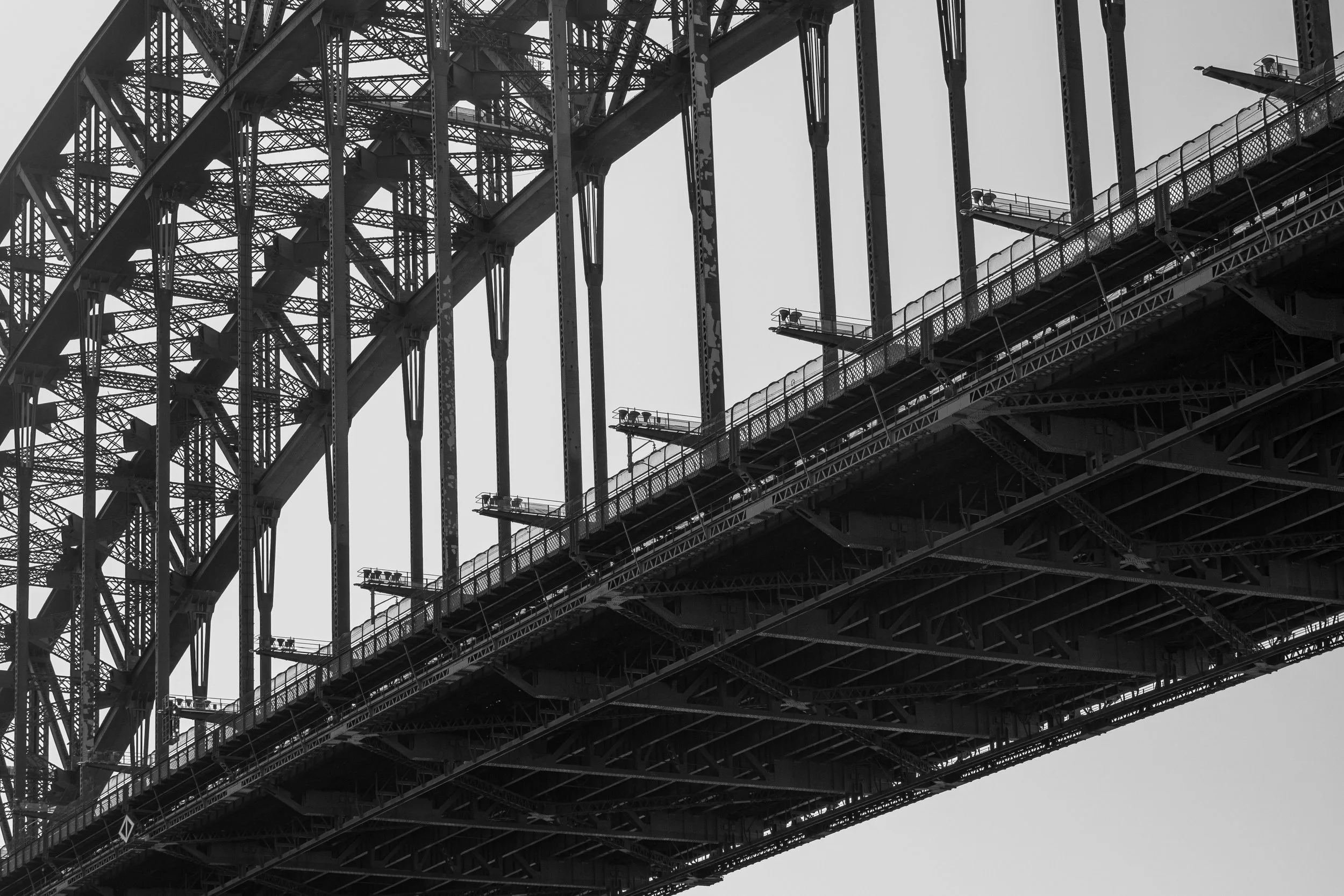 Close-up of the underside of a large steel bridge with structural supports and walkways, in black and white.