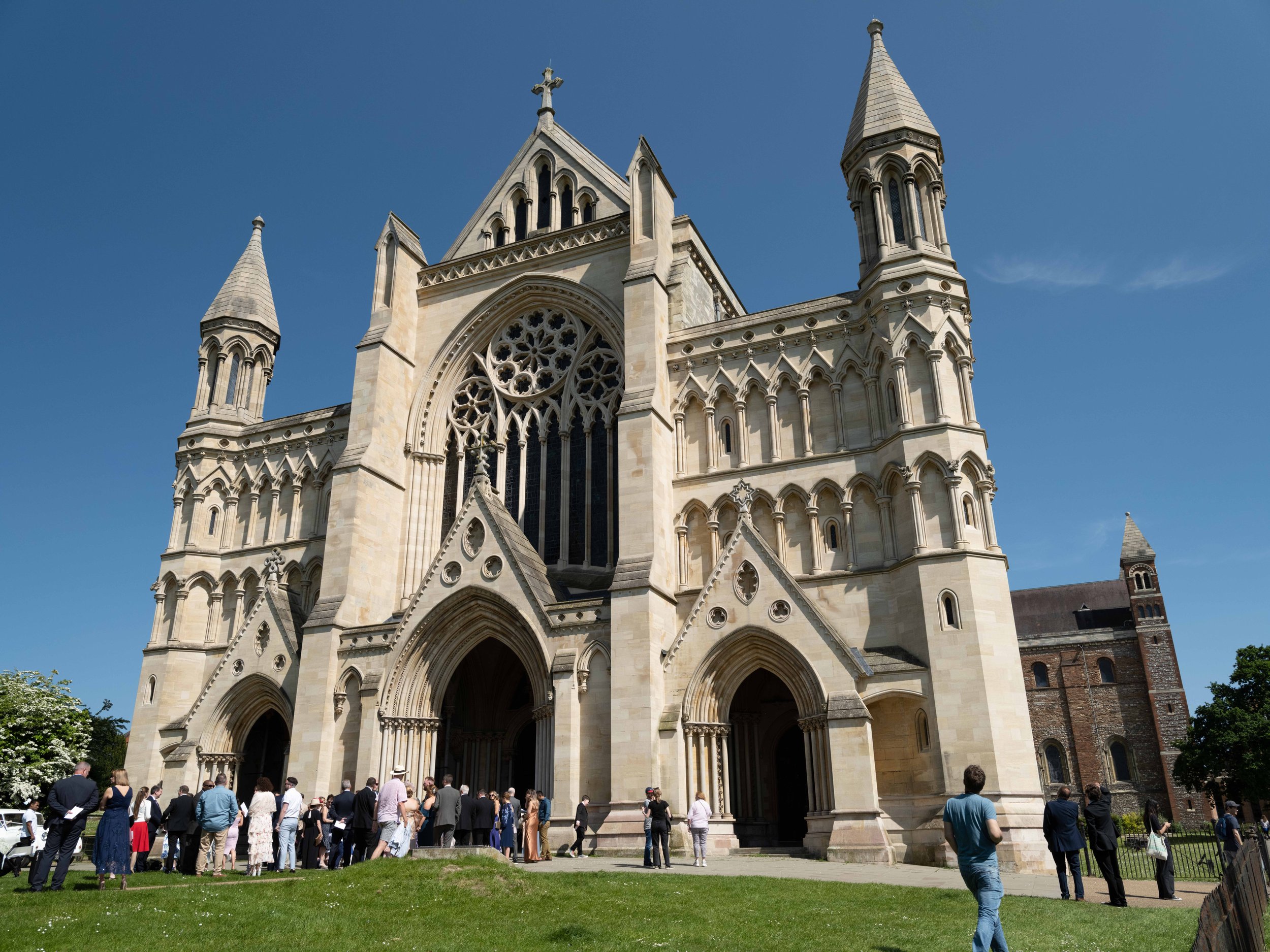 A large Gothic-style church with tall spires and intricate stonework, with a group of people gathered at the entrance on a sunny day.