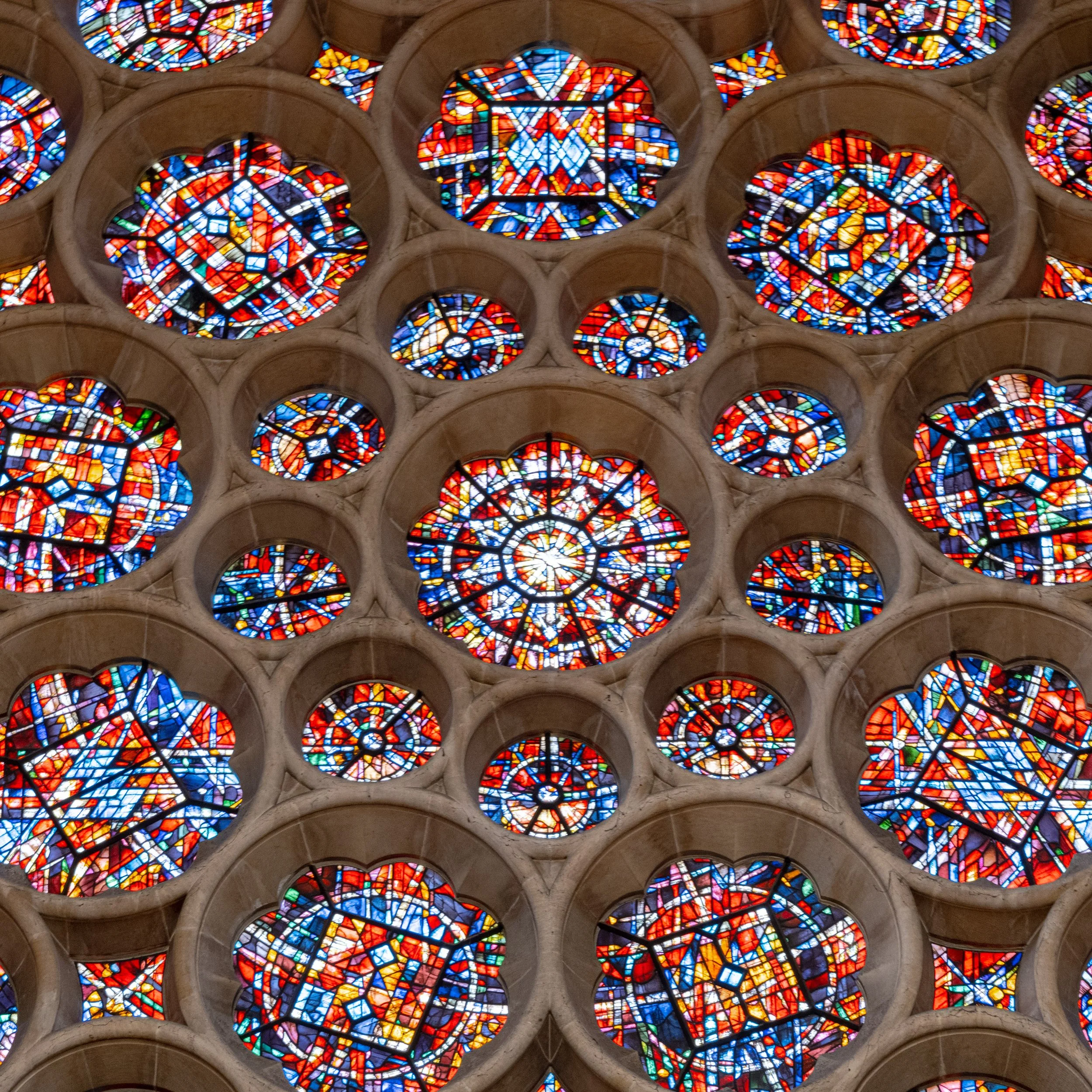 Colorful stained glass windows with intricate geometric patterns in circular and floral shapes, set within stone frames.