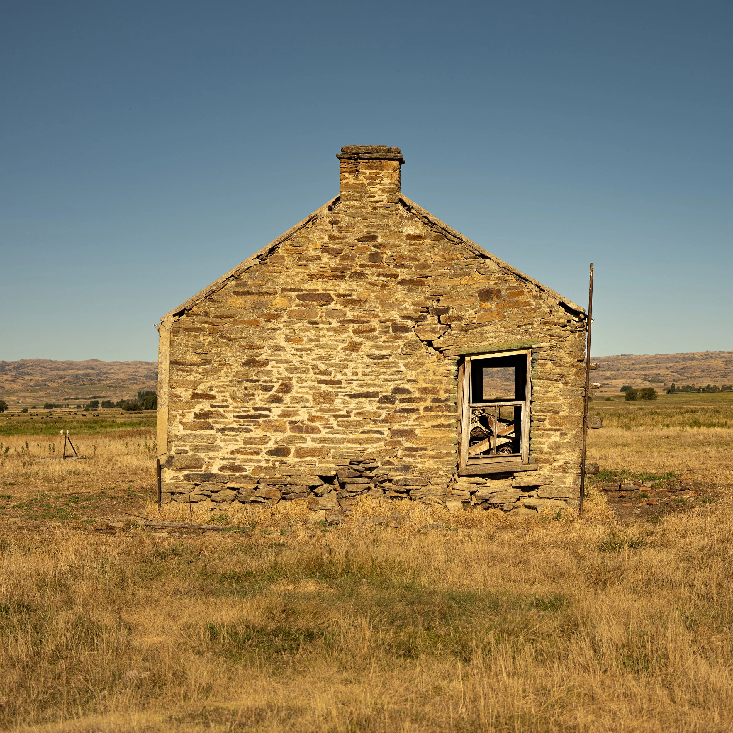 Old abandoned stone house with broken window in a field with mountains in the background.