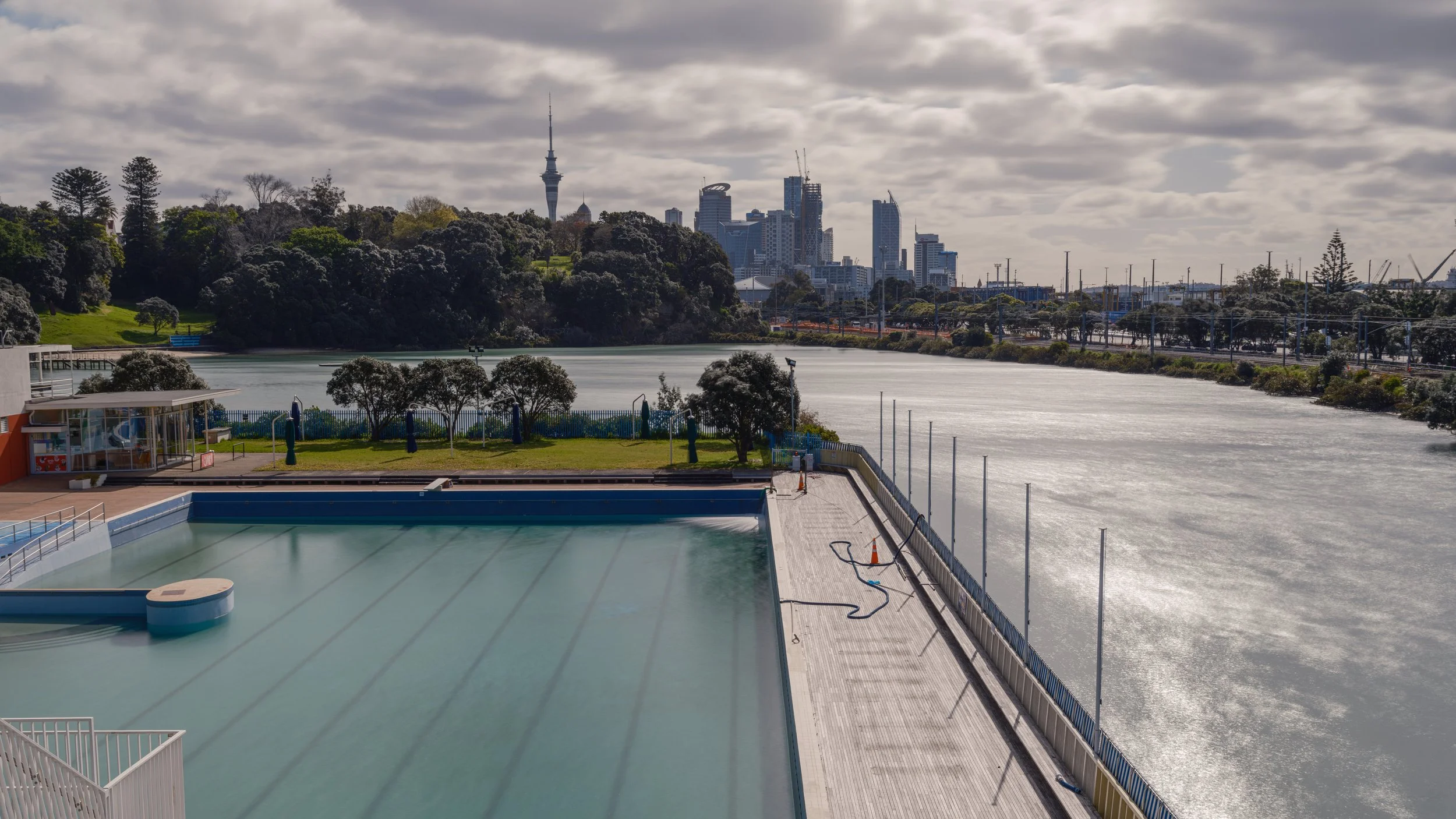 Empty outdoor swimming pool with city skyline and water view in the background.