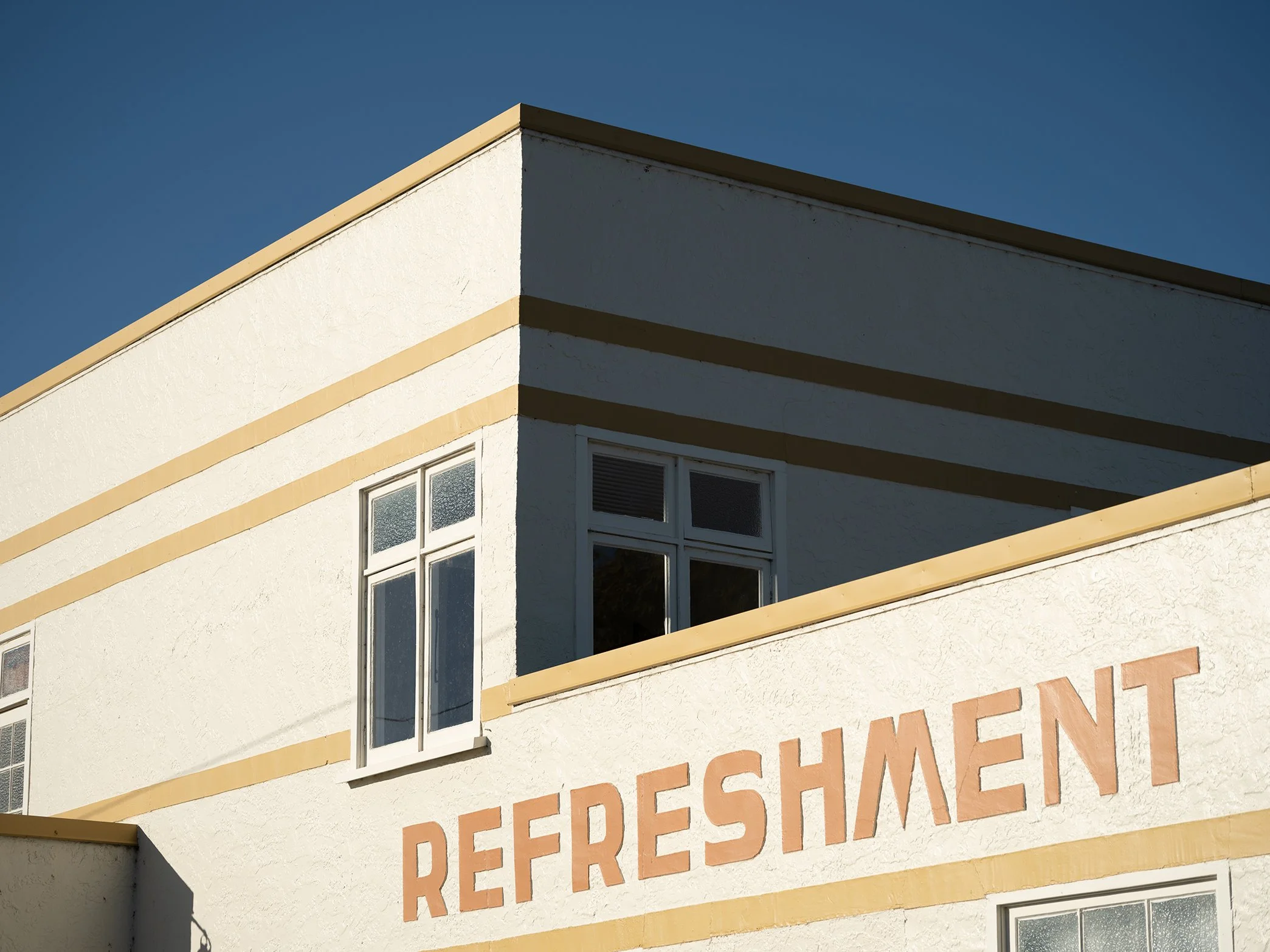Corner of a building with the word 'REFRESHMENT' painted on the exterior wall.