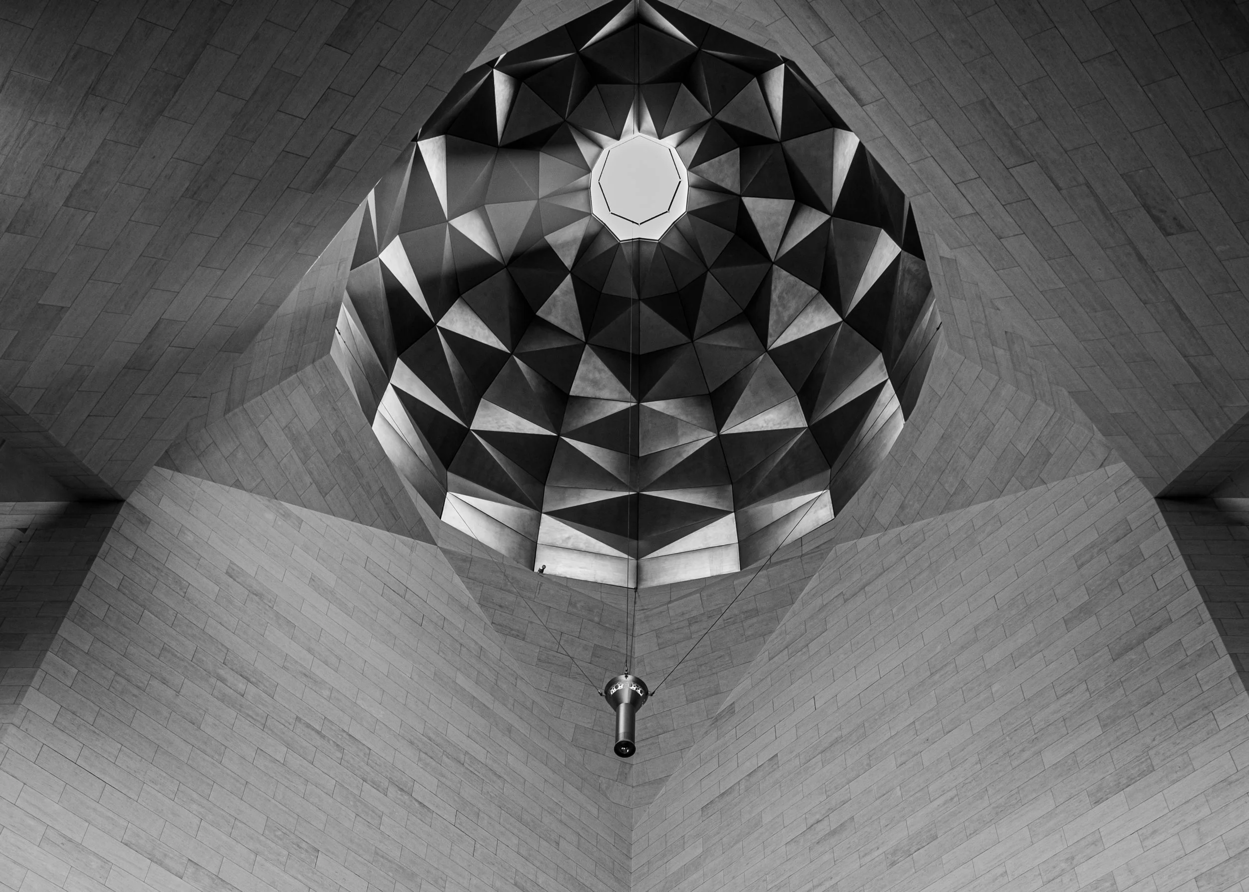 Black and white photo of an architectural ceiling with geometric patterns and a central light fixture.