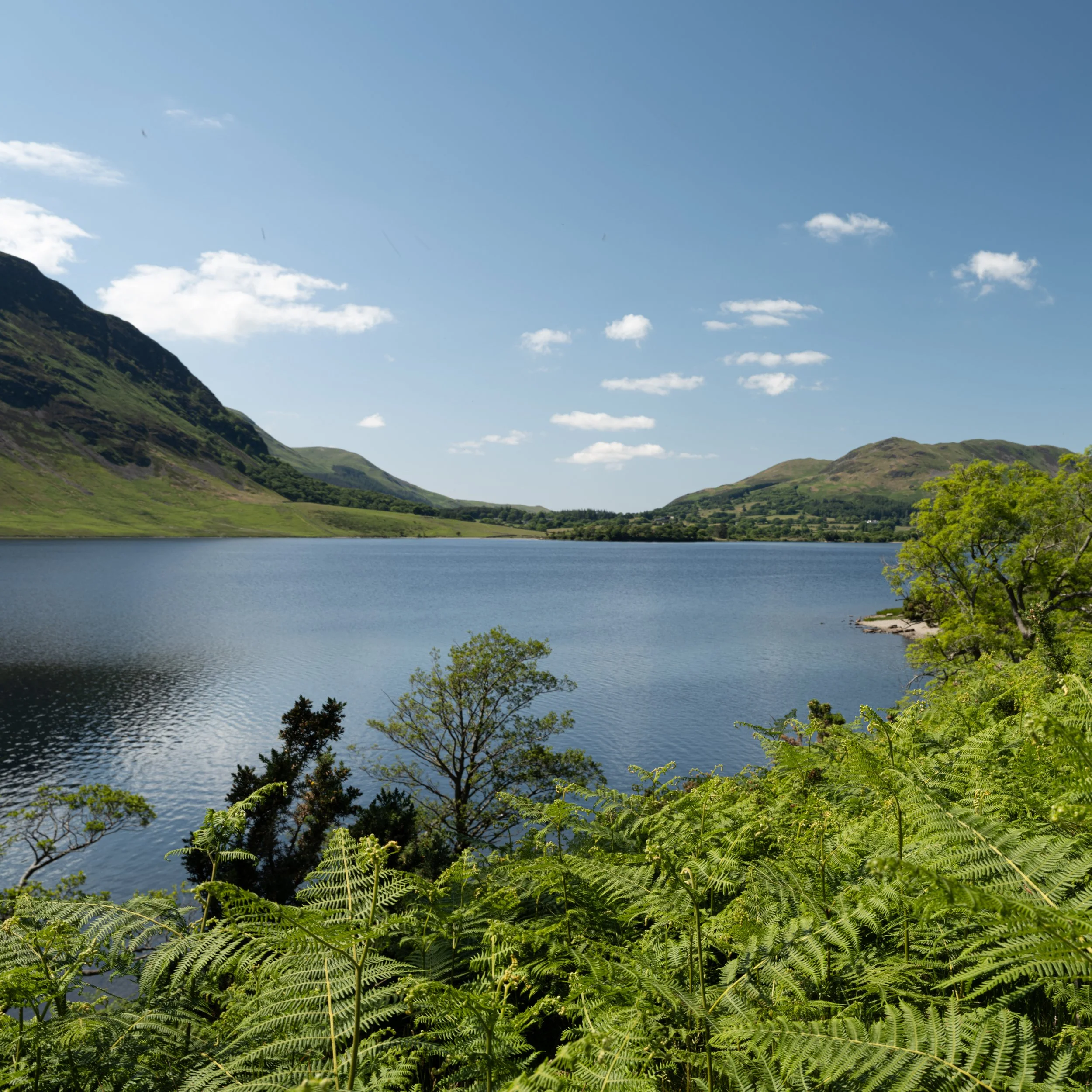 A scenic lake surrounded by lush green vegetation, mountains, and partly cloudy sky.