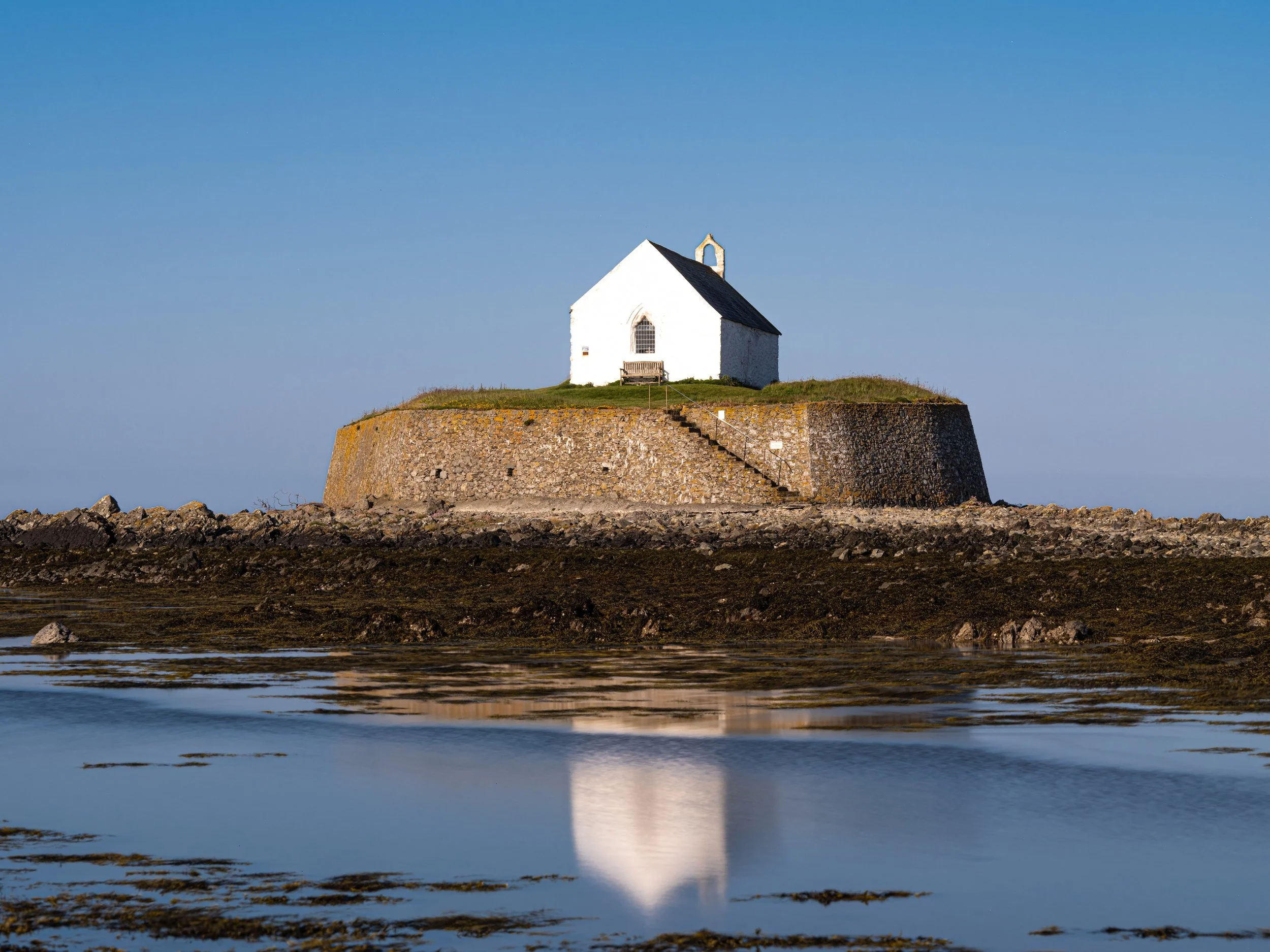 Small white church on a rocky island with clear blue sky and calm water in foreground.