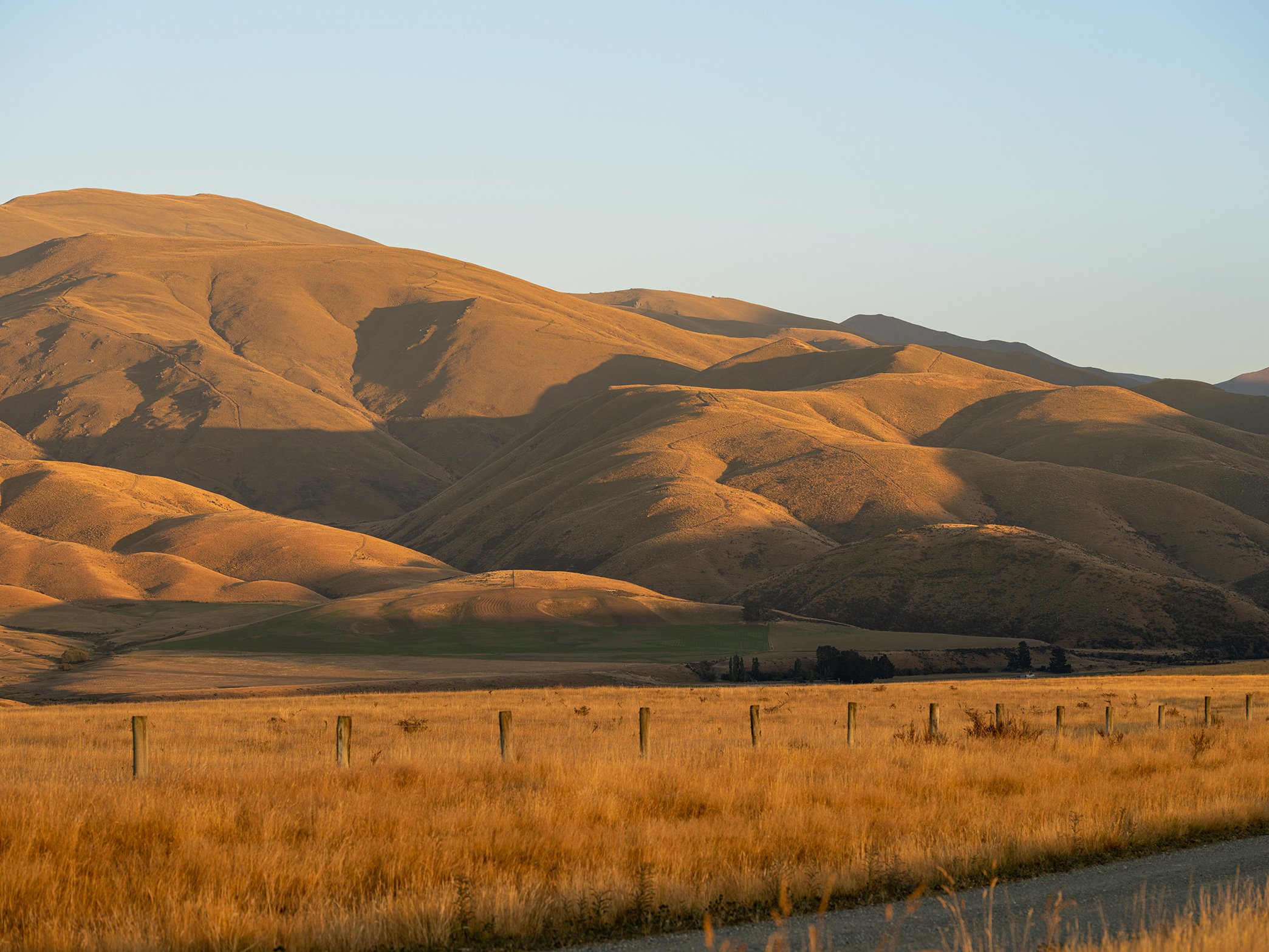 Golden rolling hills and grasslands at sunset with a fence in the foreground.