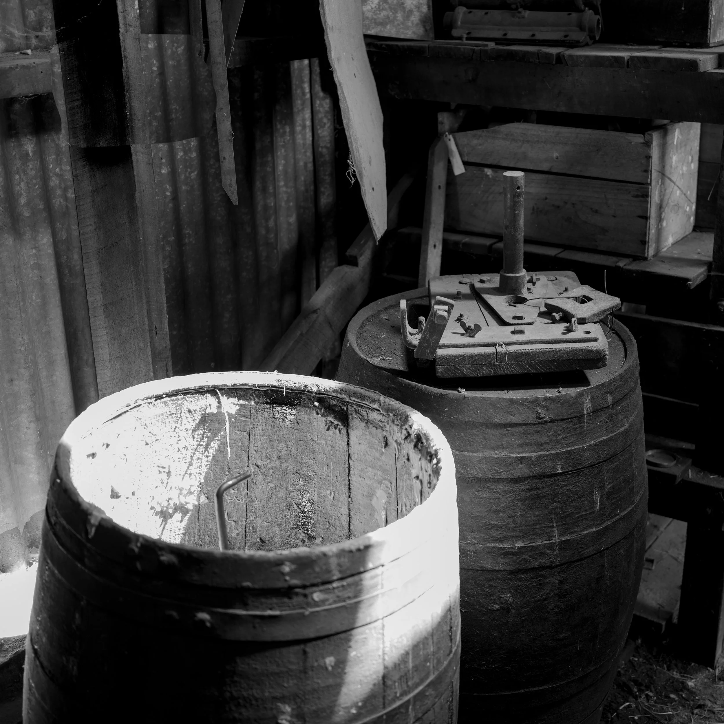 Black and white photo of two large wooden barrels in a rustic workshop, with various tools and wooden planks nearby.
