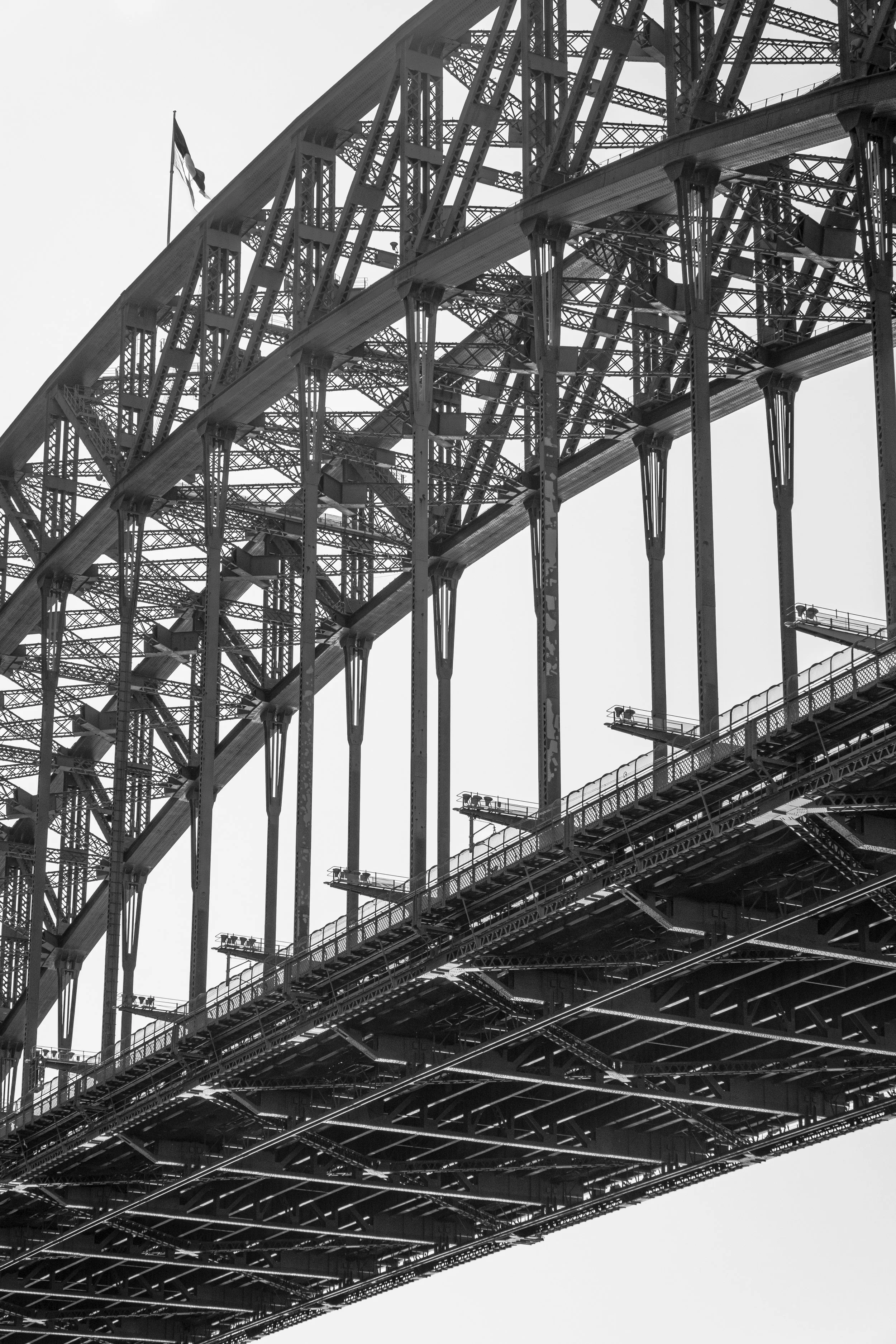 Close-up view of the structural steel framework of an arched bridge in black and white, with a flag flying at the top.