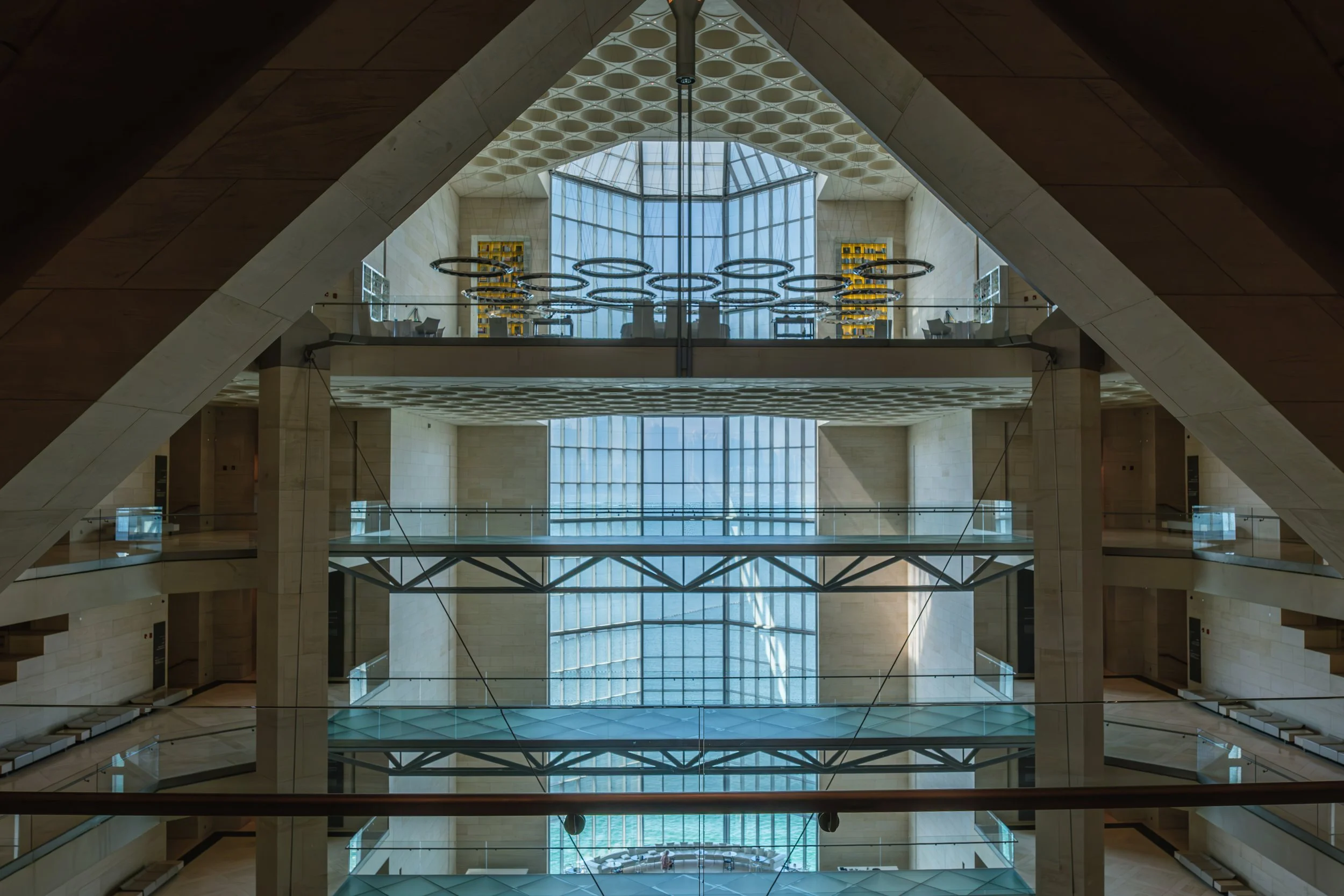 Interior view of a modern multi-story building with glass windows, circular lighting fixtures, and sky bridges connecting different floors.