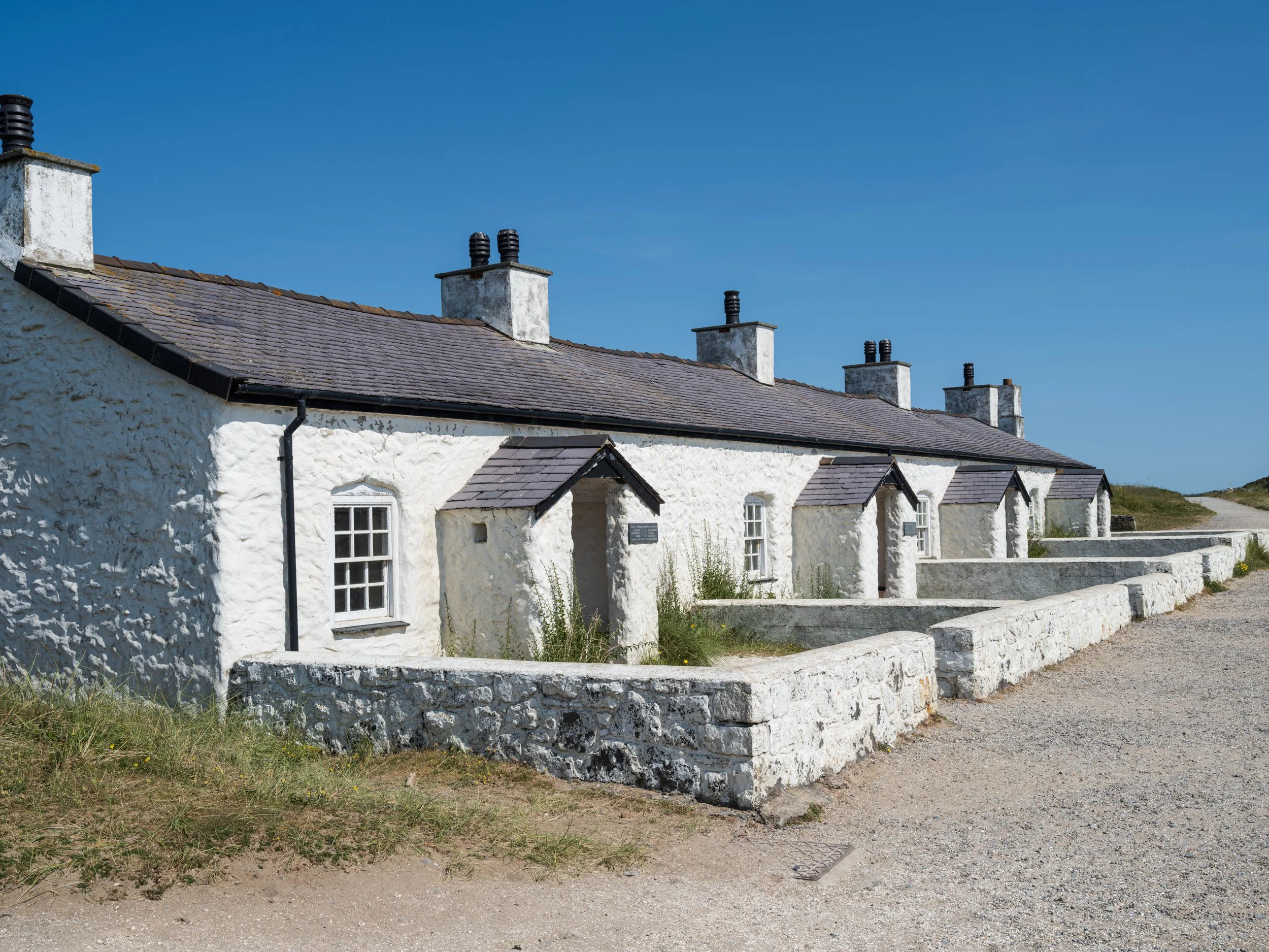 Row of white cottages with slate roofs and chimneys under a blue sky