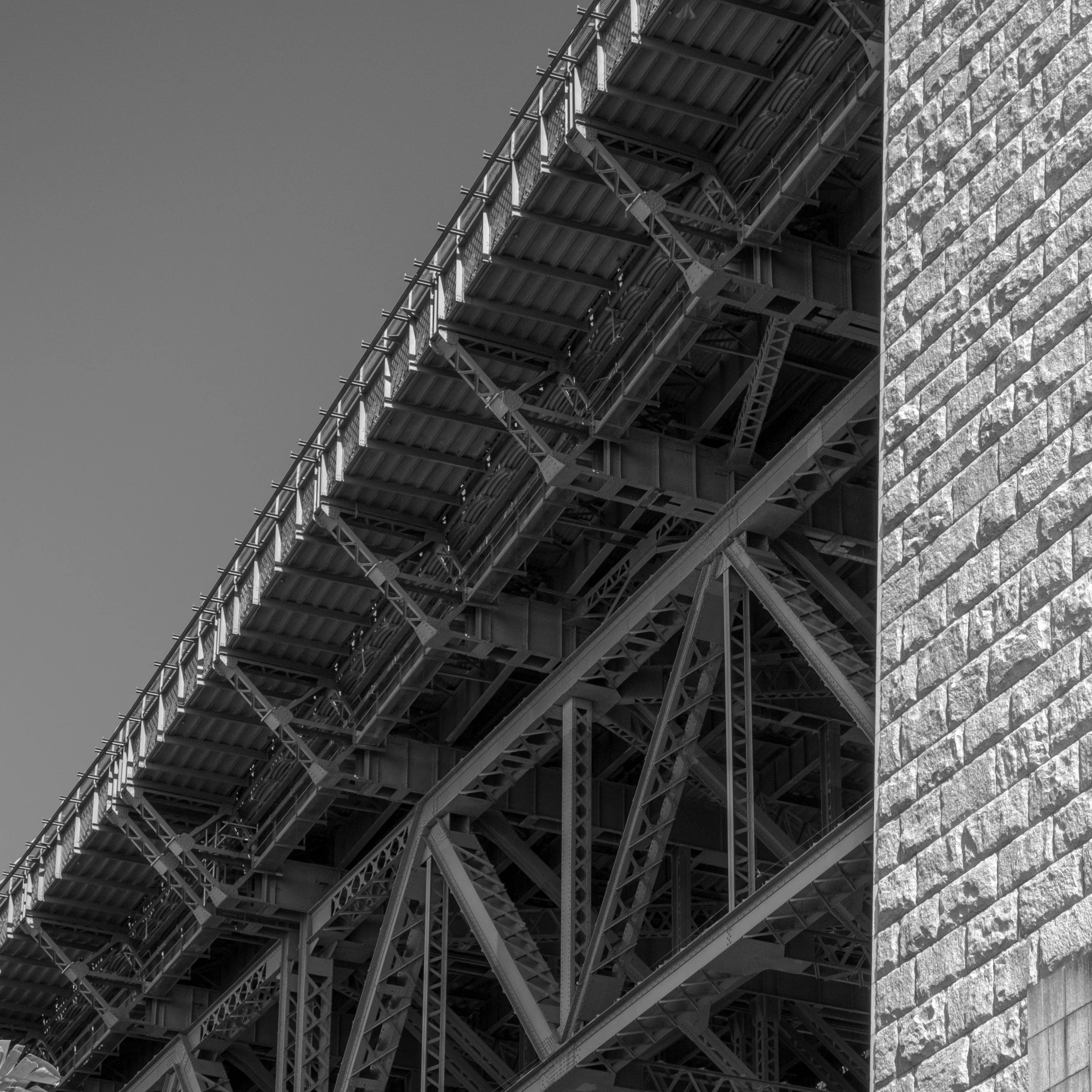 Close-up of a large steel bridge structure with detailed metal beams, girders, and supports against a clear sky, black and white photograph.