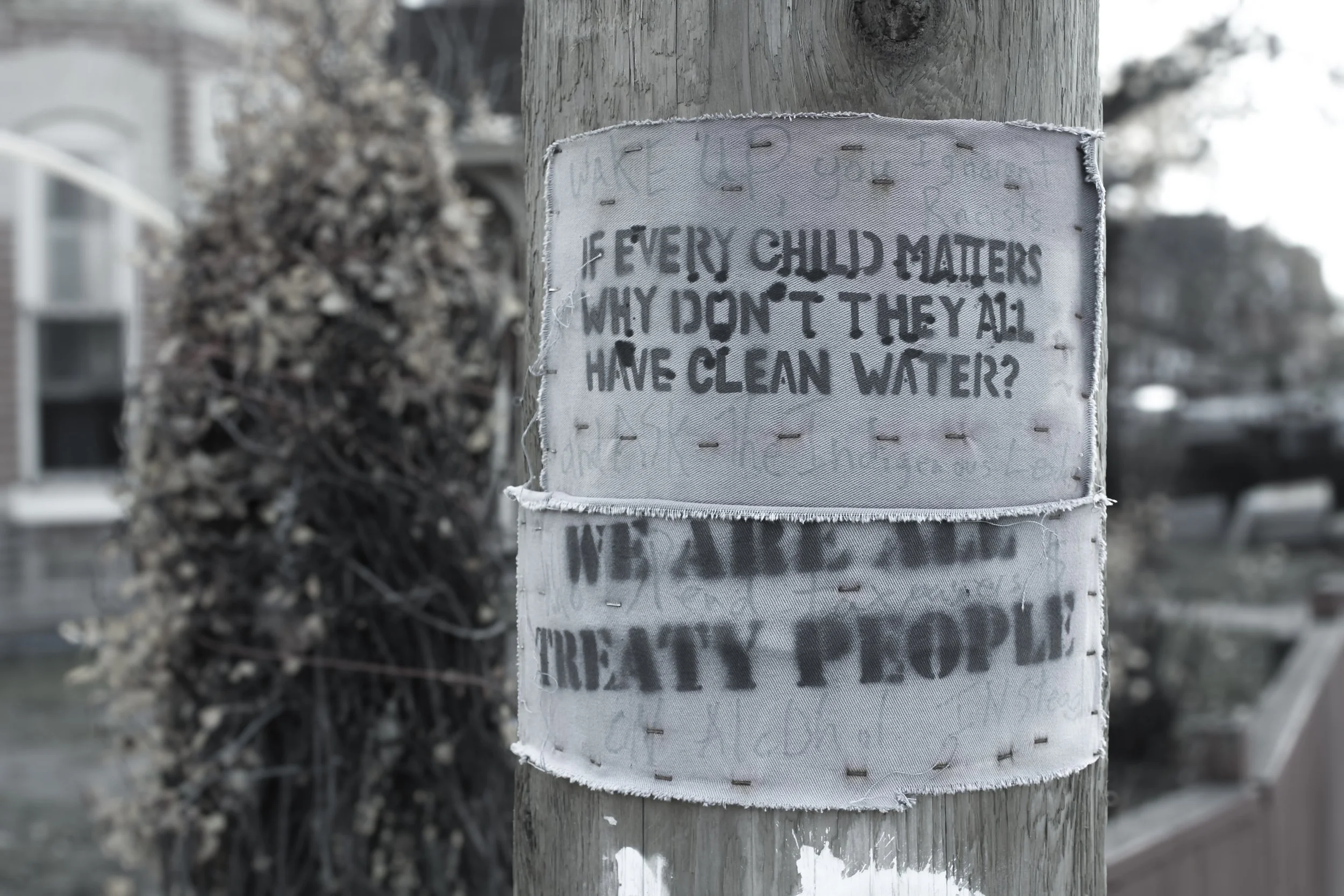 photo of a post on the street that has two signs stapled to it that read "if every child matters why don't they all have clean water" and "we are all treaty people"