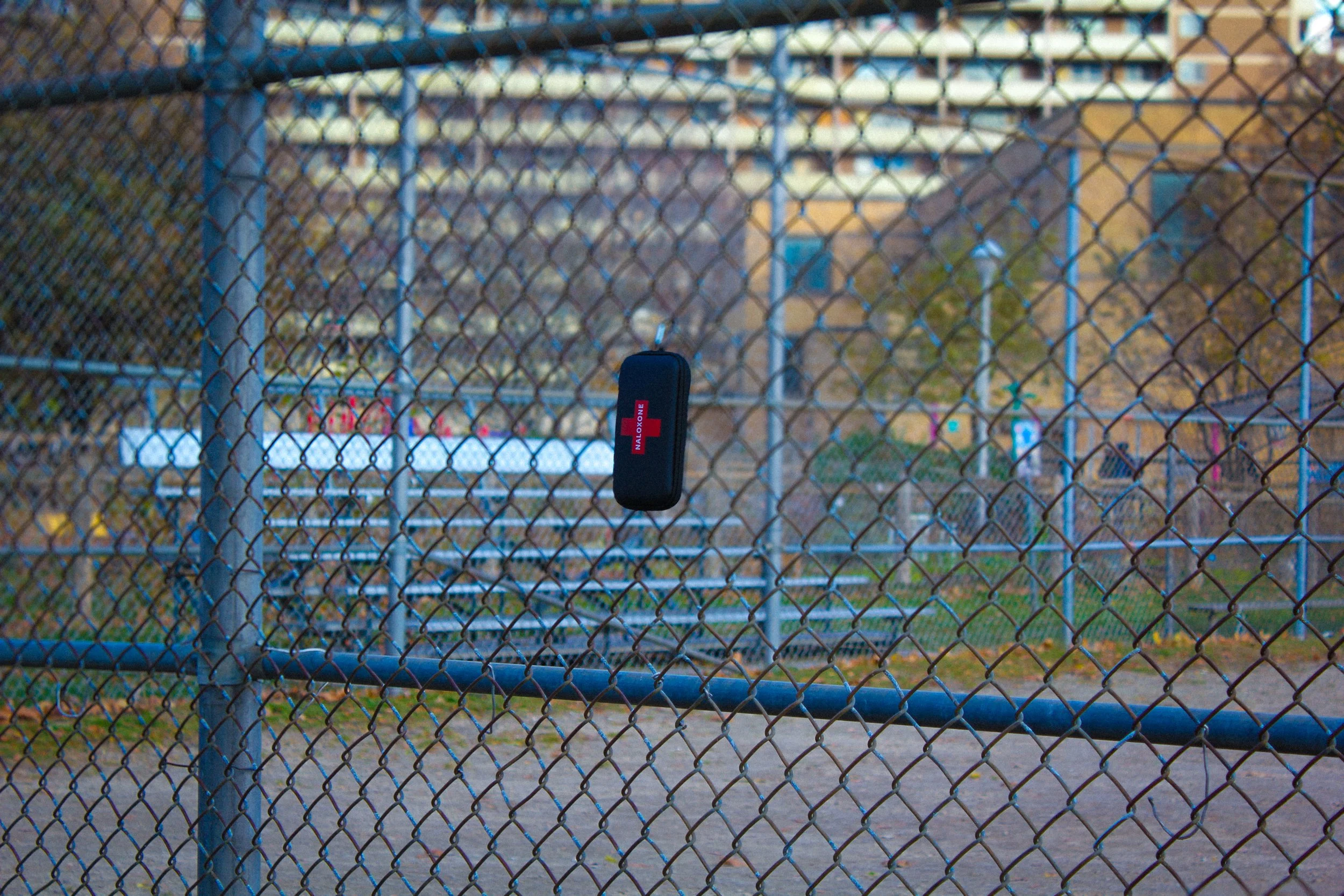 photo of a narcan kit hooked onto a chain link fence at a baseball diamond