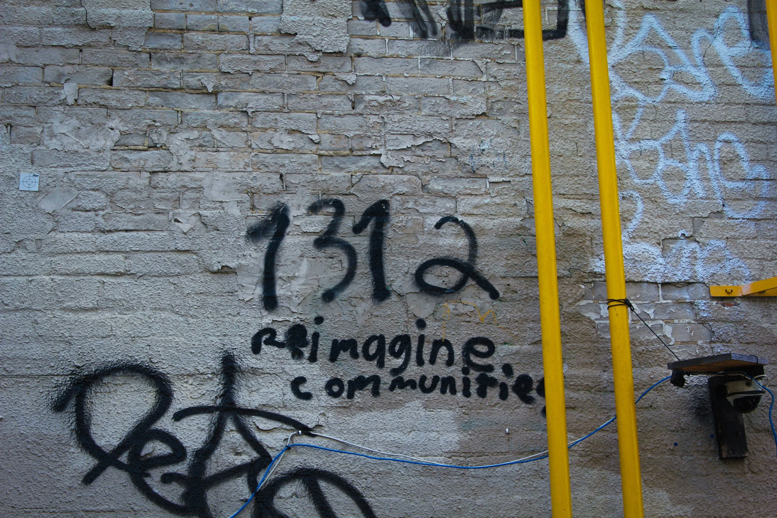 photo of a wall with black spray paint that reads "1312 reimagine communities"