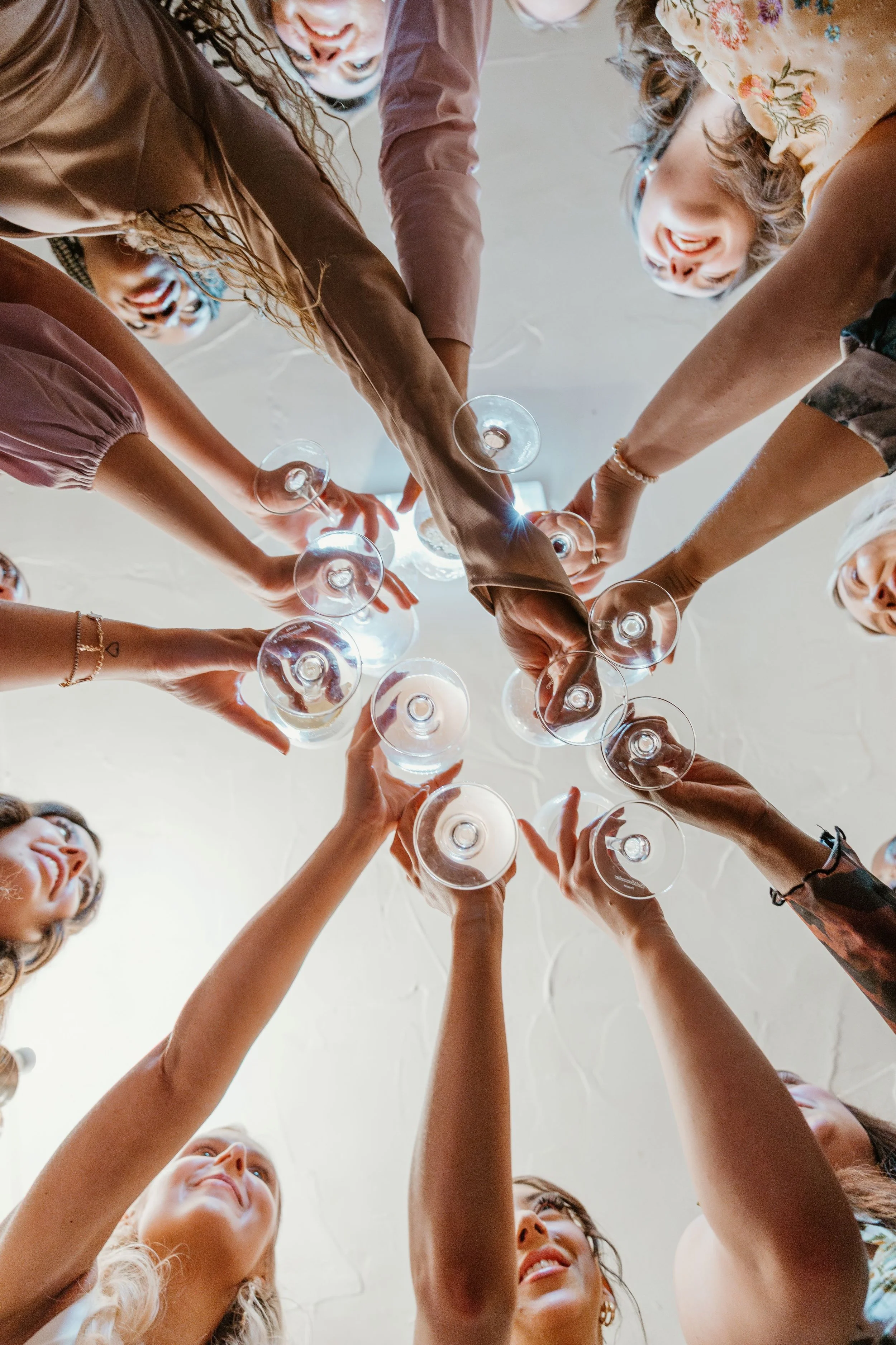 A group of people gathering and connecting in a circle, raising glasses for a toast, seen from below.
