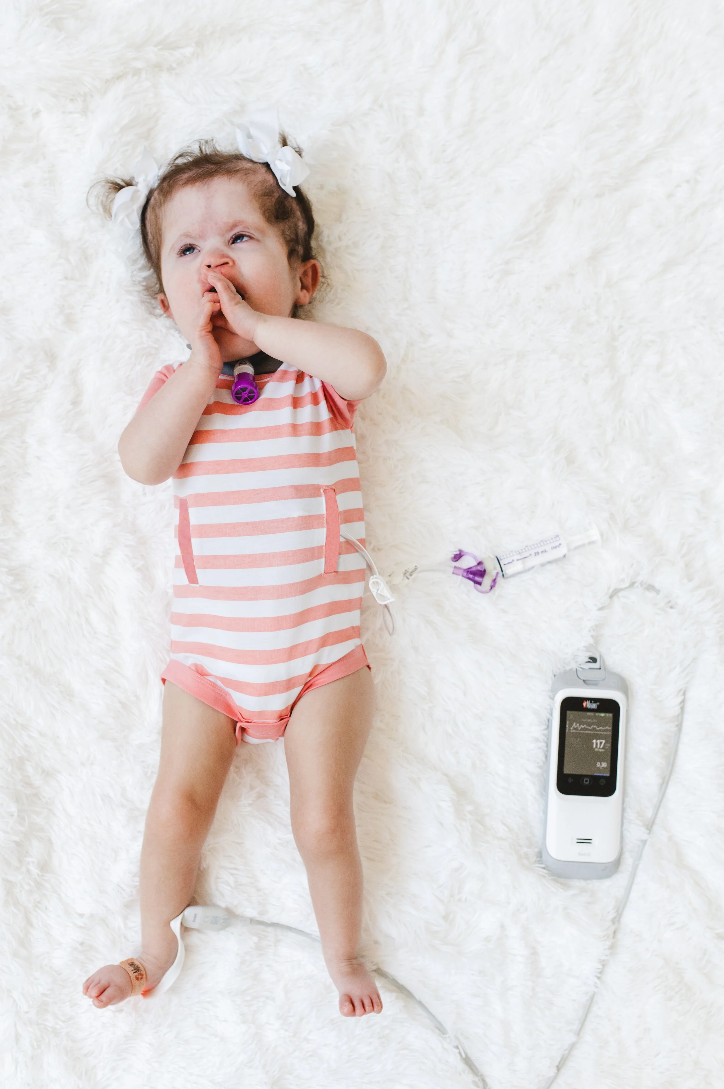 Young girl lying on a white fluffy surface, with medical monitoring equipment nearby.