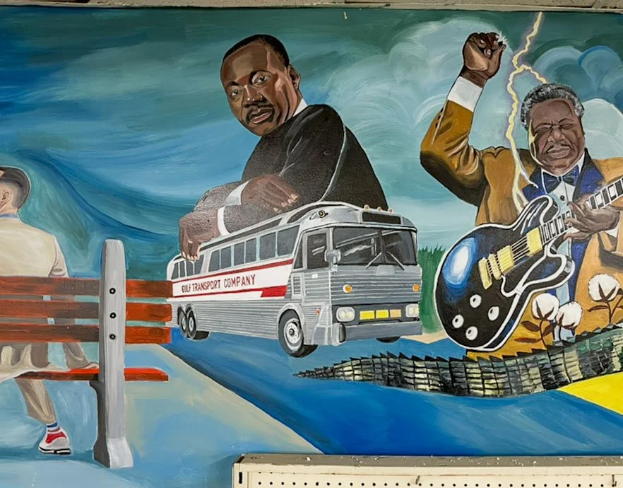 back of Forest Gump sitting on bench on left side, Martin Luther King Jr. with arms folded over Gulf Transport Company bus in center, Lightnin' Hopkins playing guitar on right side, alligator tail in lower right corner under cotton plants