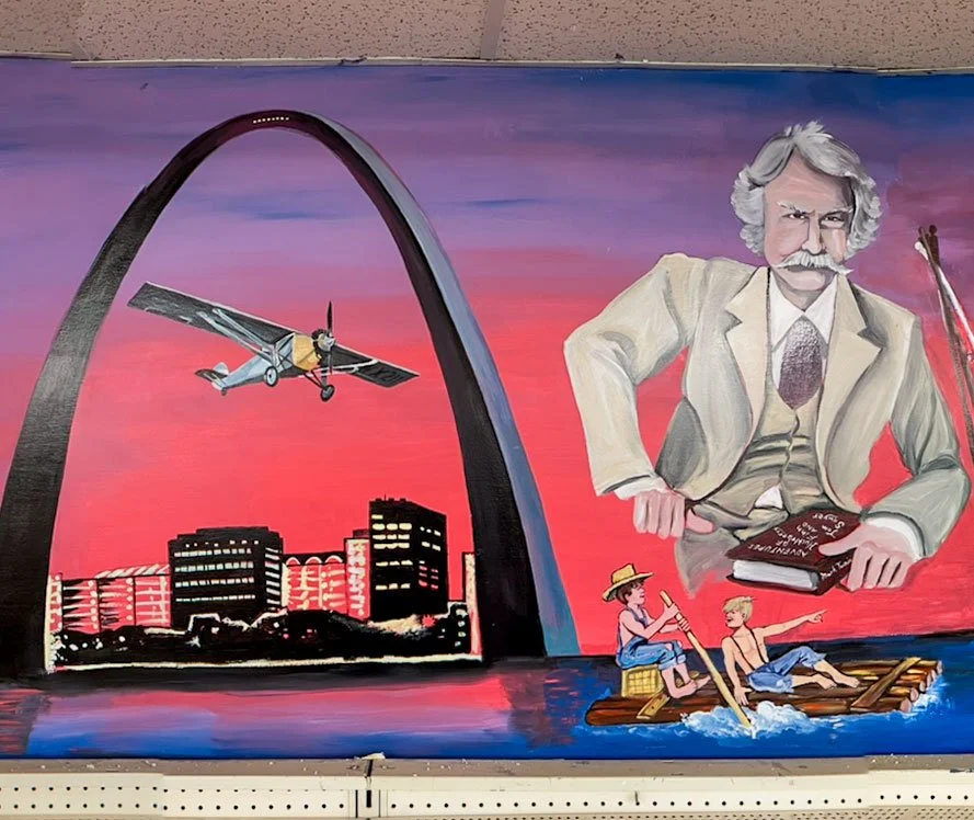 Gateway Arch above St. Louis skyline on left side, Spirit Of St. Louis plane flying through it, Mark Twain on upper right side holding book, Tom Sawyer and Huckleberry Finn on raft under him
