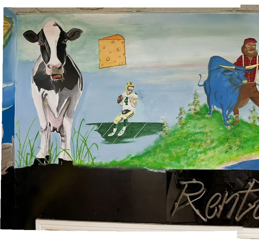 Cow on left side, wedge of cheese to its right above Brett Favre, Babe the Blue Ox and Paul Bunyan walking down a hill on right side, rental sign underneath them