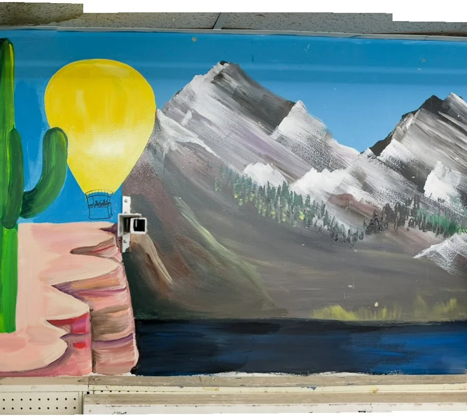 cactus on left edge, with hot air balloon next to it, mountains in center and right side of image